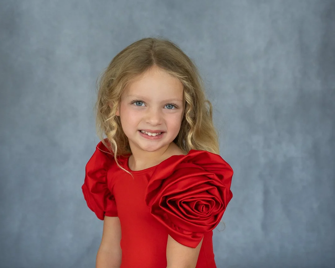 Beautiful child with blond hair with banana curls in a red dress with puffy sleeves.