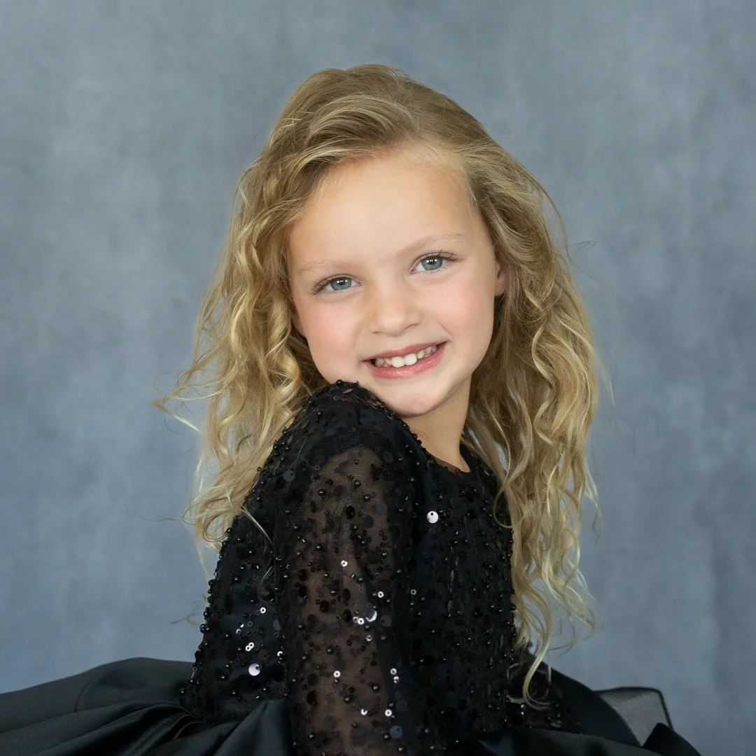 Beautiful child with long blond hair, in a back sparkling pageant dress. Pageant photo for little miss NC