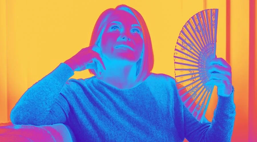 Person with short hair sitting, holding a fan in a vibrant, colorful setting.