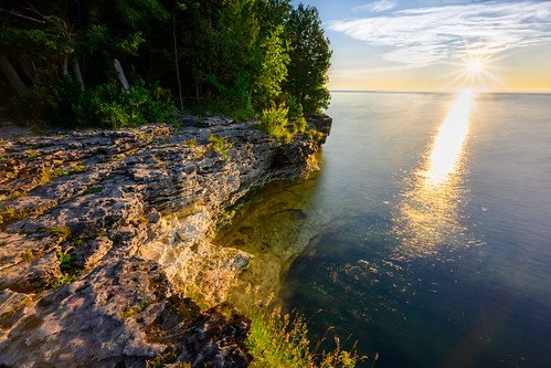 Sunset over a rocky lakeshore with trees on the left