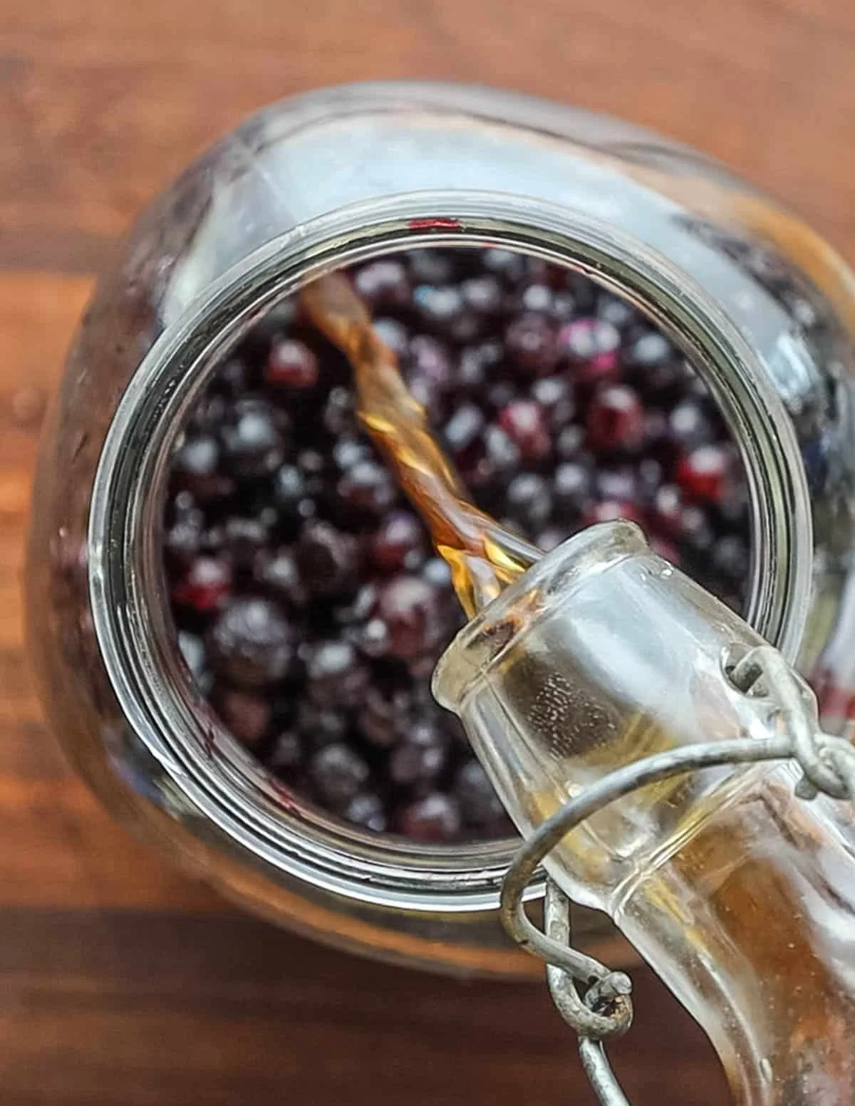 Homemade blueberry liqueur being poured over fresh blueberries in a glass jar
