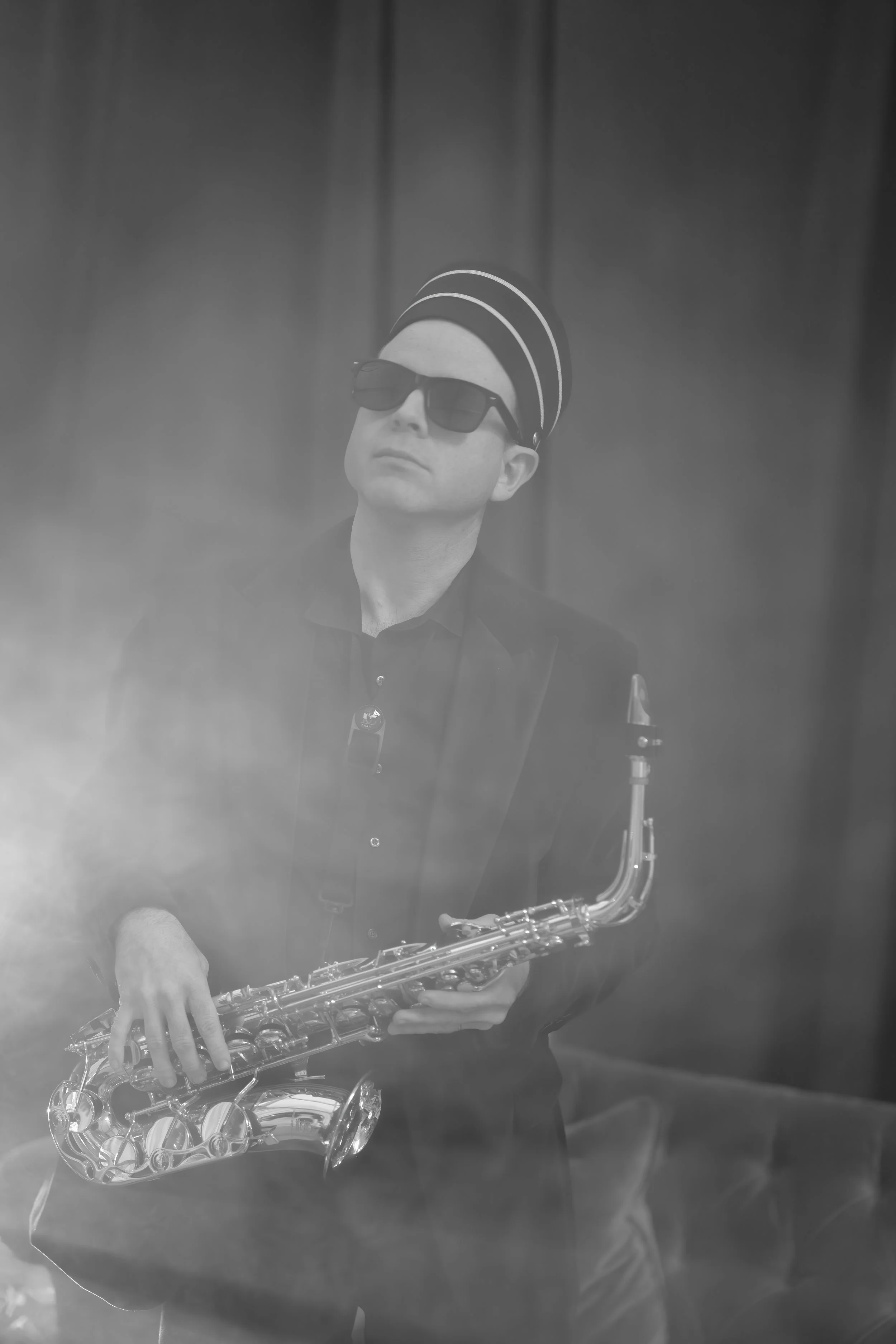 A man wearing dark sunglasses and a striped hat playing a saxophone.