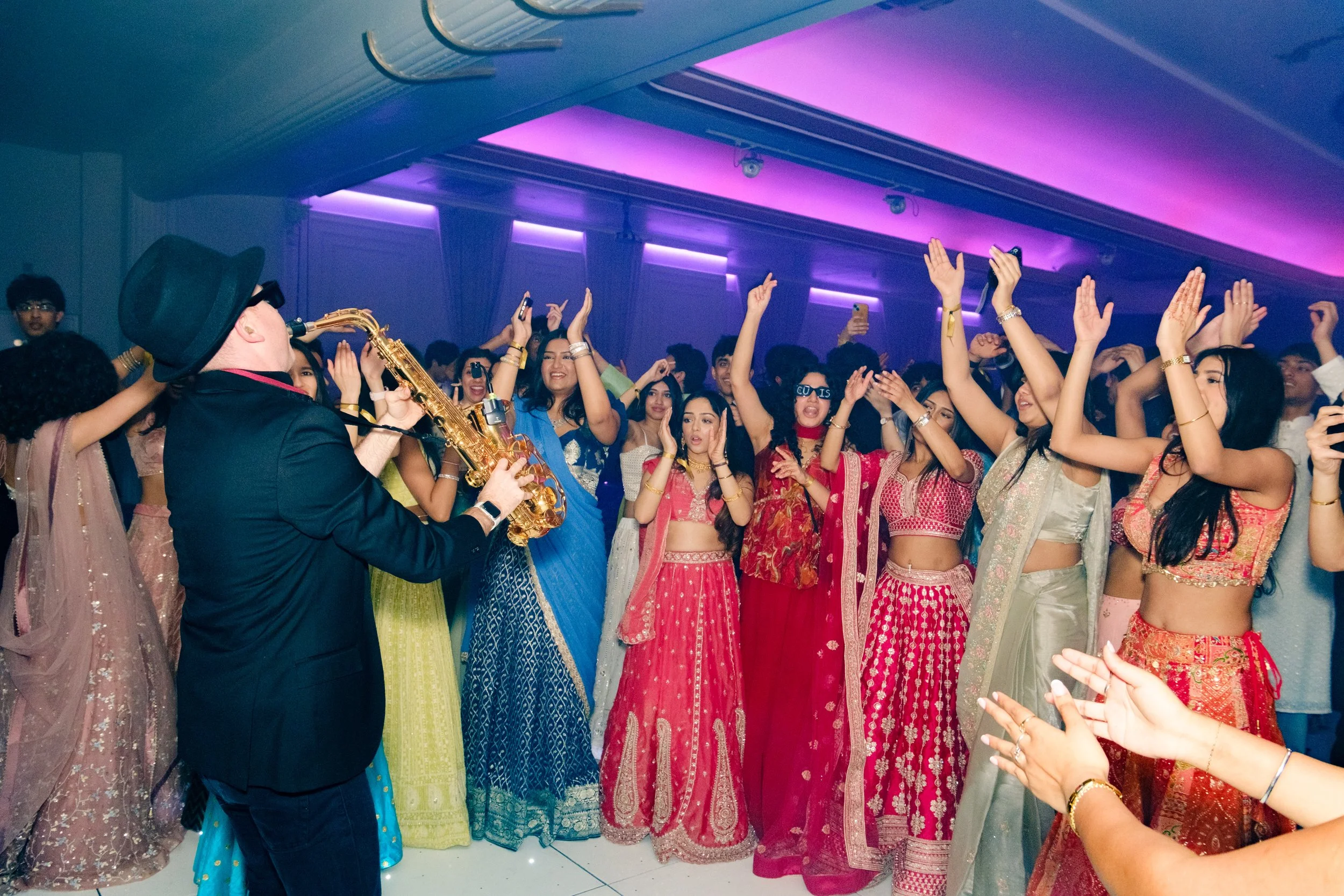 Group of women in colorful sarees and a musician playing a saxophone at a celebration.