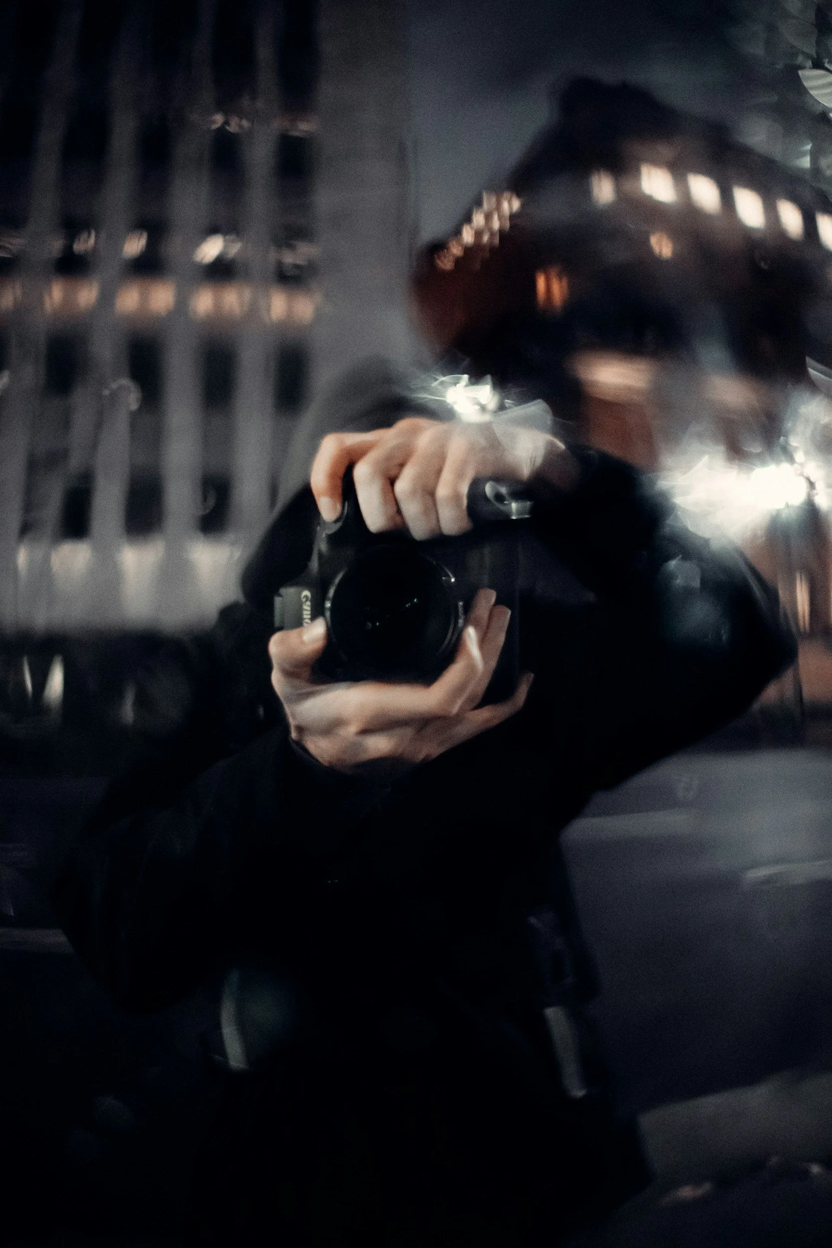 A person taking a mirror selfie with a camera in a dimly lit elevator, with metal walls and lighting reflections.