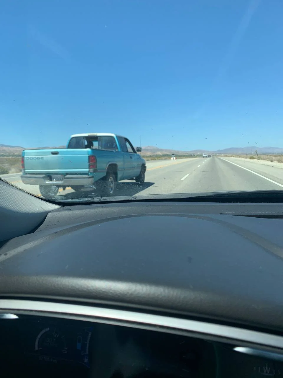 View of a blue pickup truck driving on a highway in a desert landscape under a clear blue sky.