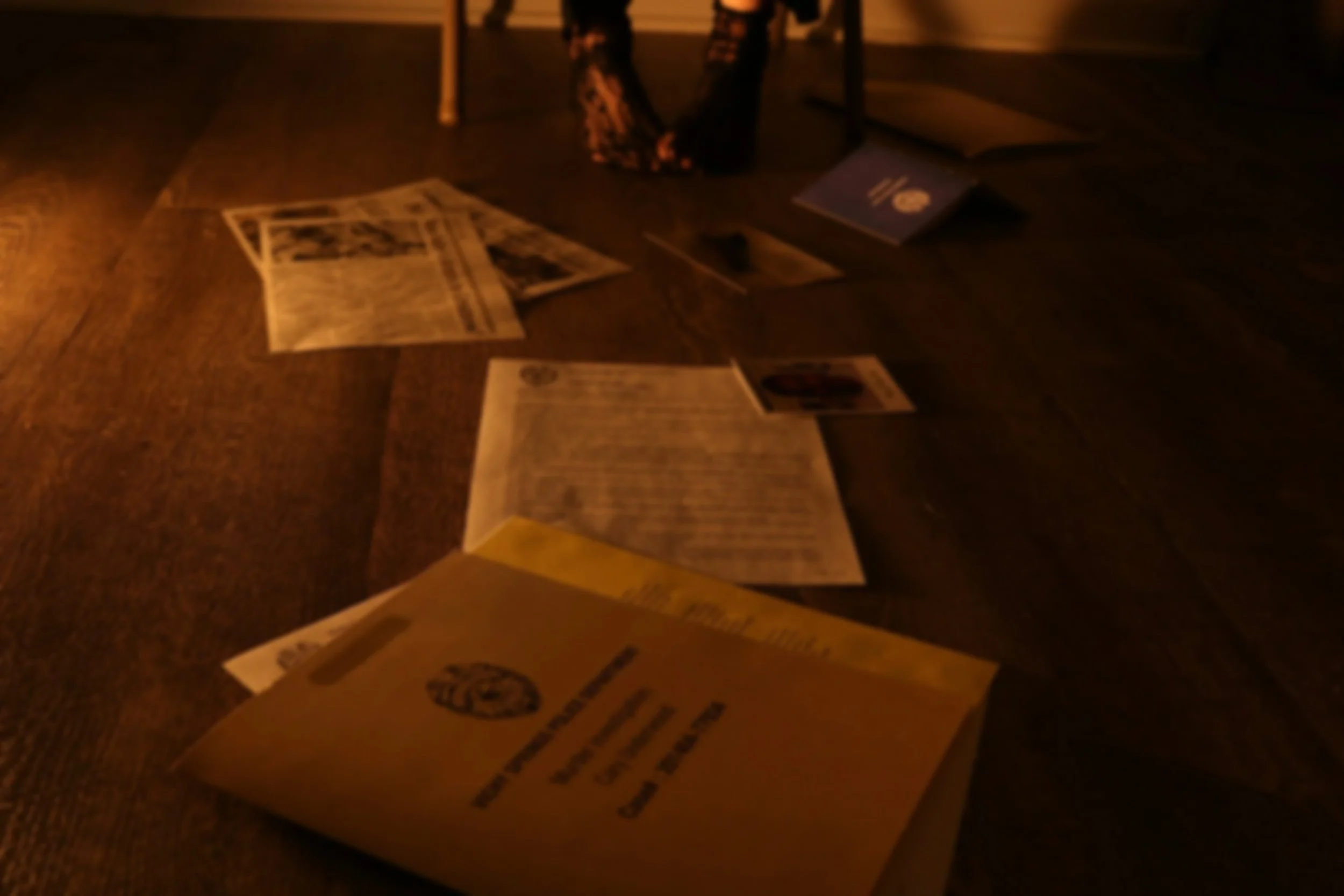 A cardboard box on a wooden surface with scattered newspapers and a purple book, and a bag in the background, dimly lit.