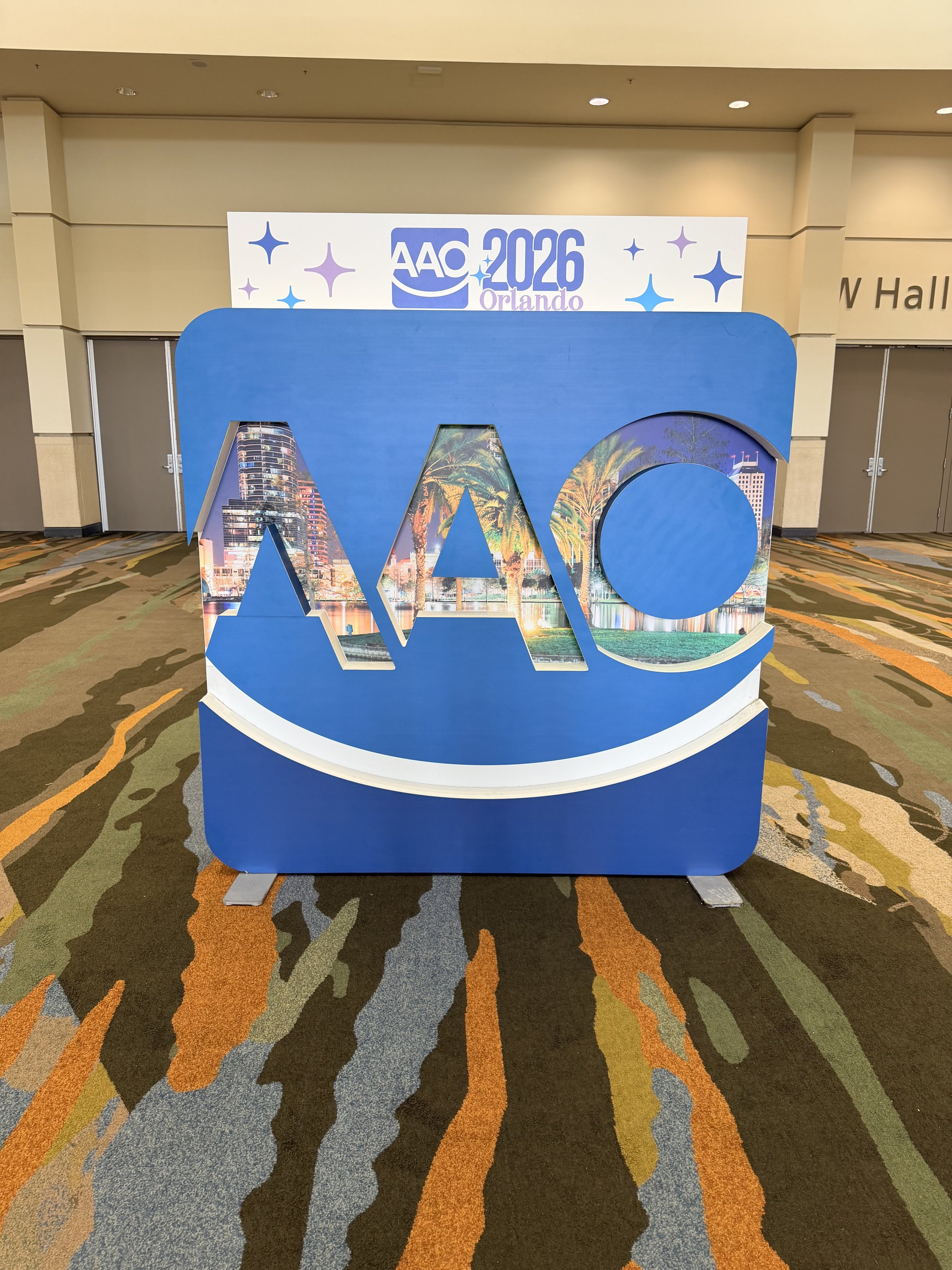 Large decorative display with the letters A, W, and C, featuring images of cityscapes and palm trees inside the letters, placed on a patterned carpet, with a backdrop indicating the AAO 2026 Orlando conference.