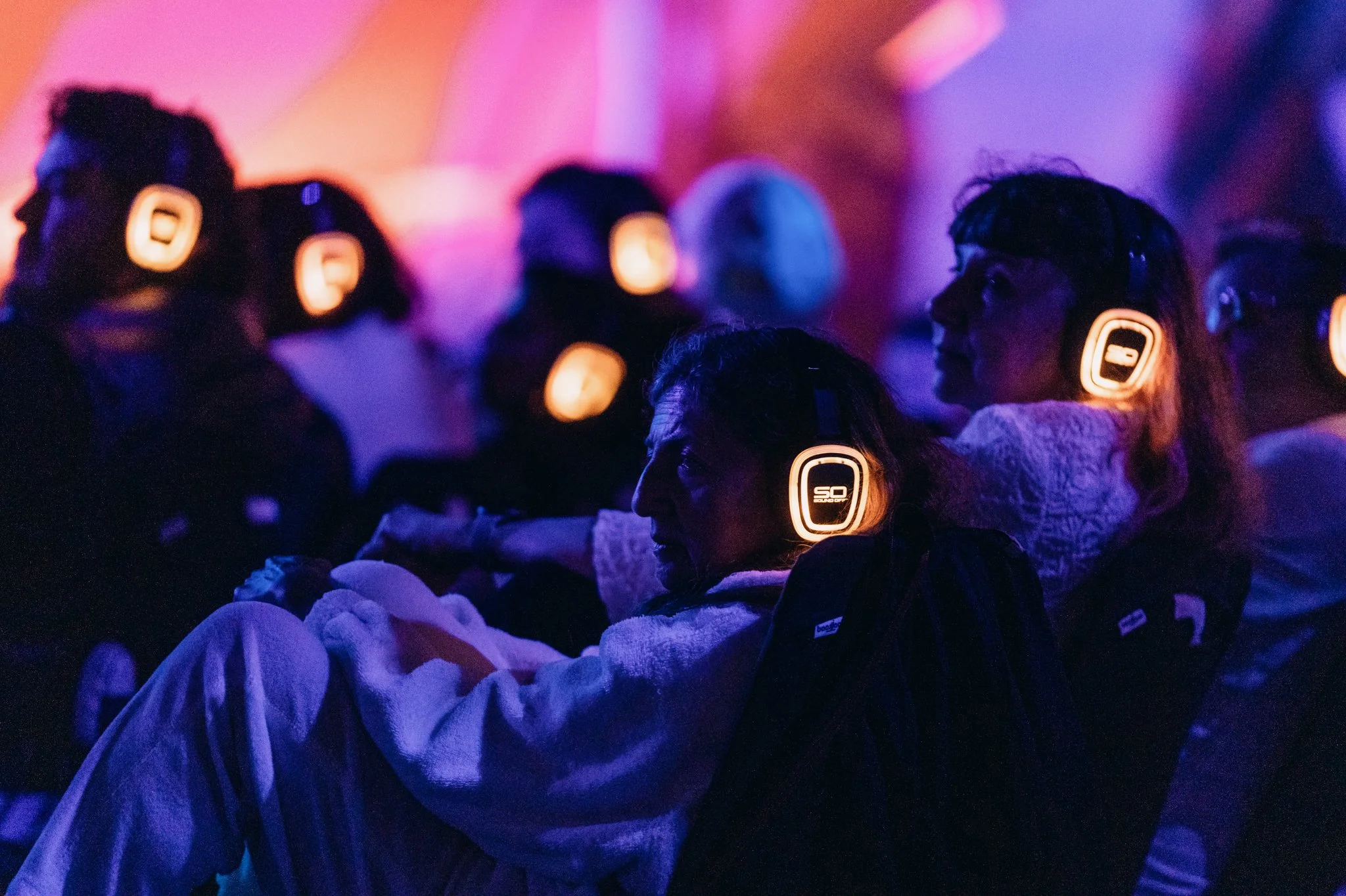 Group of people wearing illuminated radio-frequency silent headphones at an outdoor immersive music and theater event.