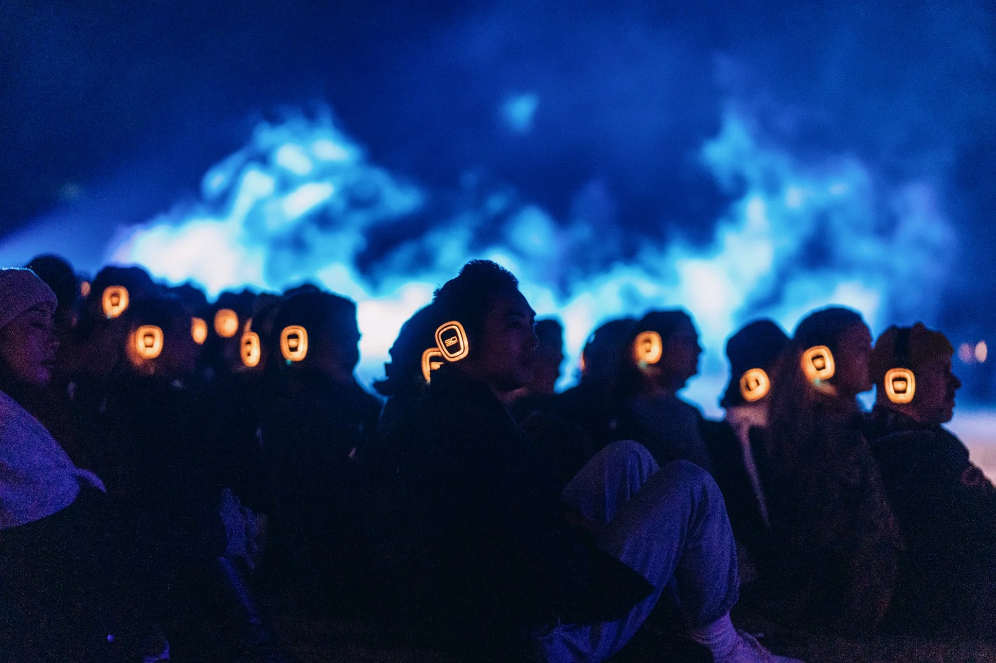 Audience members wearing silent disco RF headsets illuminated orange in a dark environment with blue lighting and a smoky backdrop.