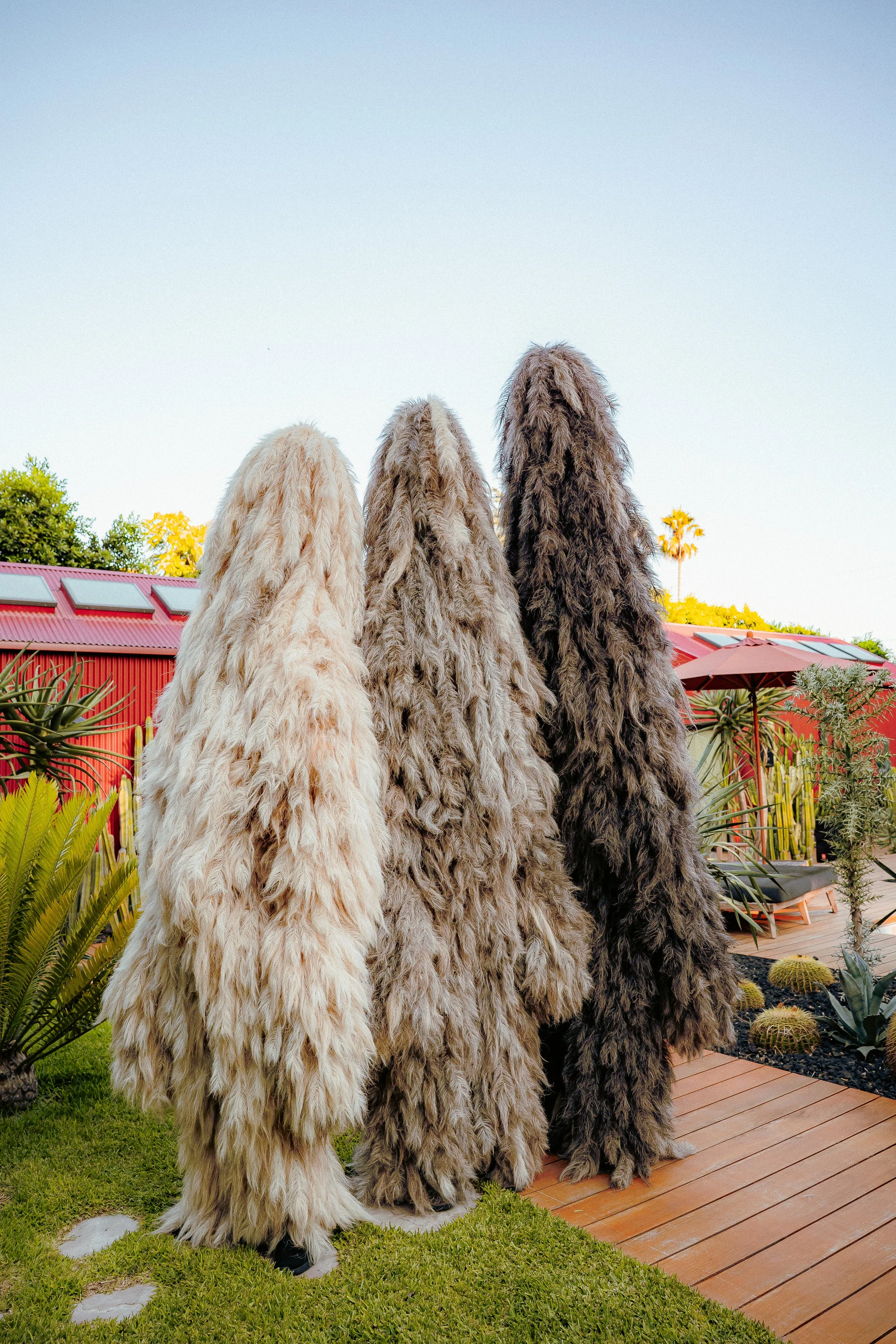 Three large-scale archetypal furry leviathan figures stand outdoors on a grassy area.