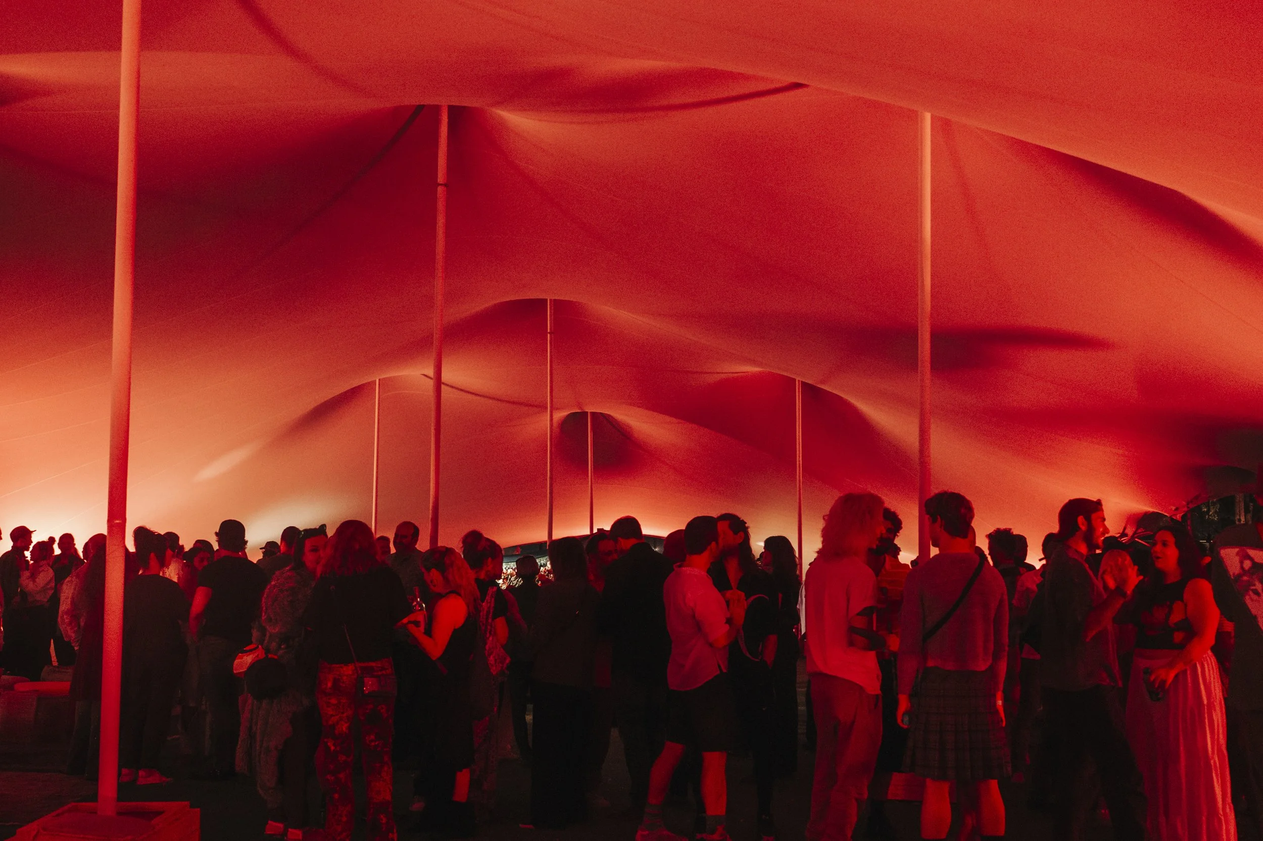 People gathered and engaged in conversation inside a large Bedouin stretch tent with red artistic lighting.
