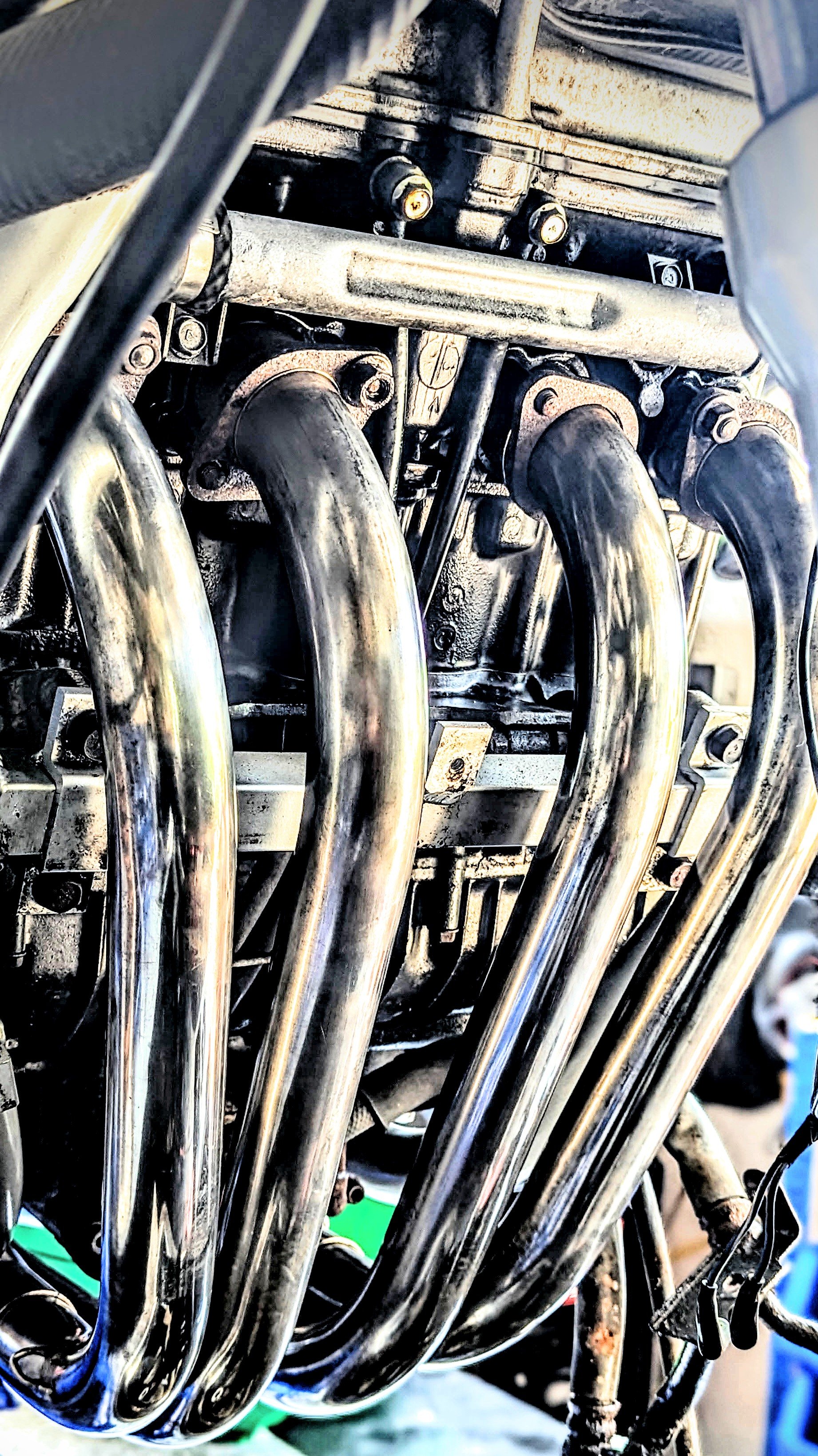 Close-up of a vintage car engine showing six shiny exhaust headers and engine components.