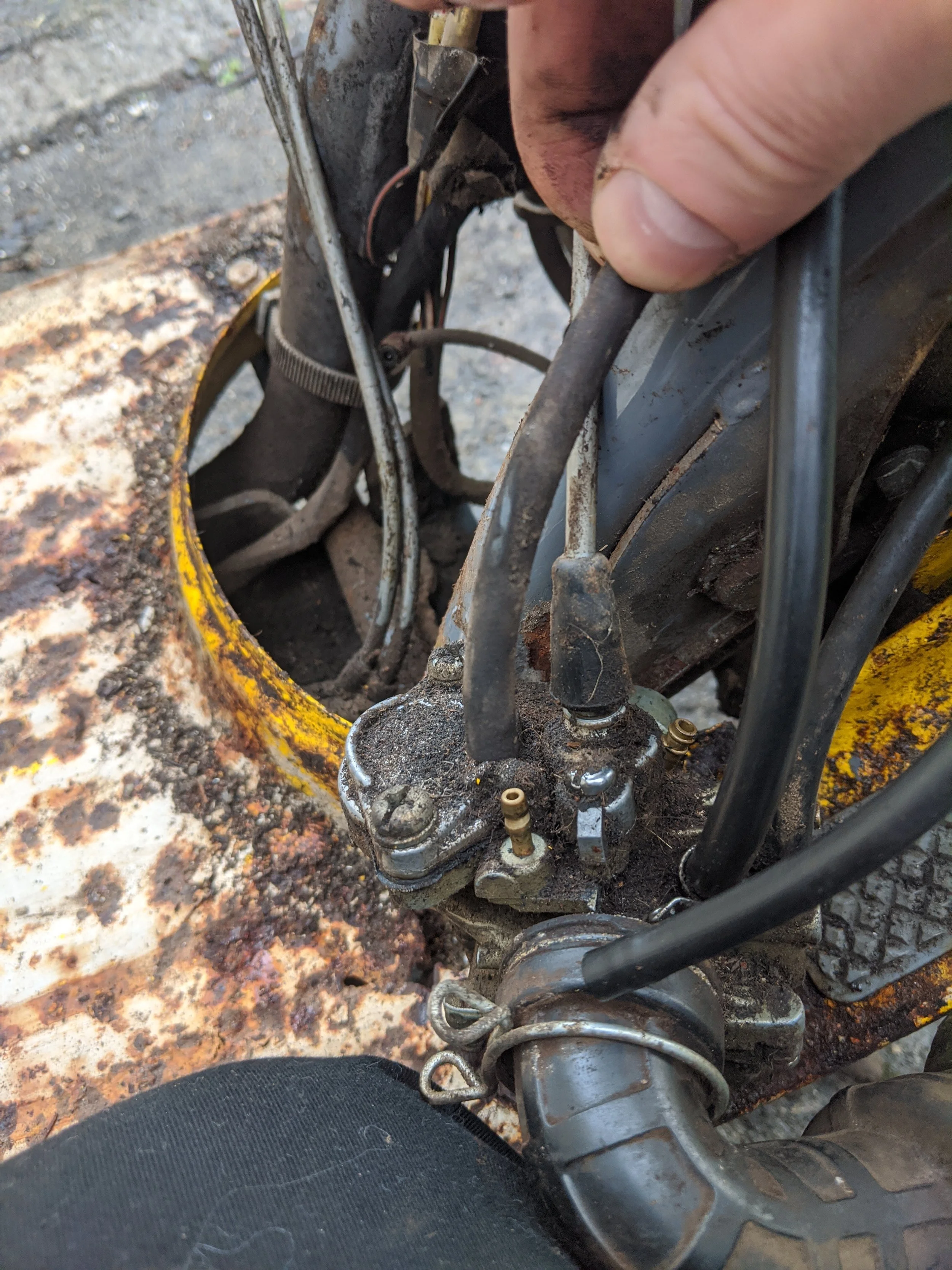 Close-up of a motorcycle engine and frame with a person's hand working on it, on a rusty metal surface.