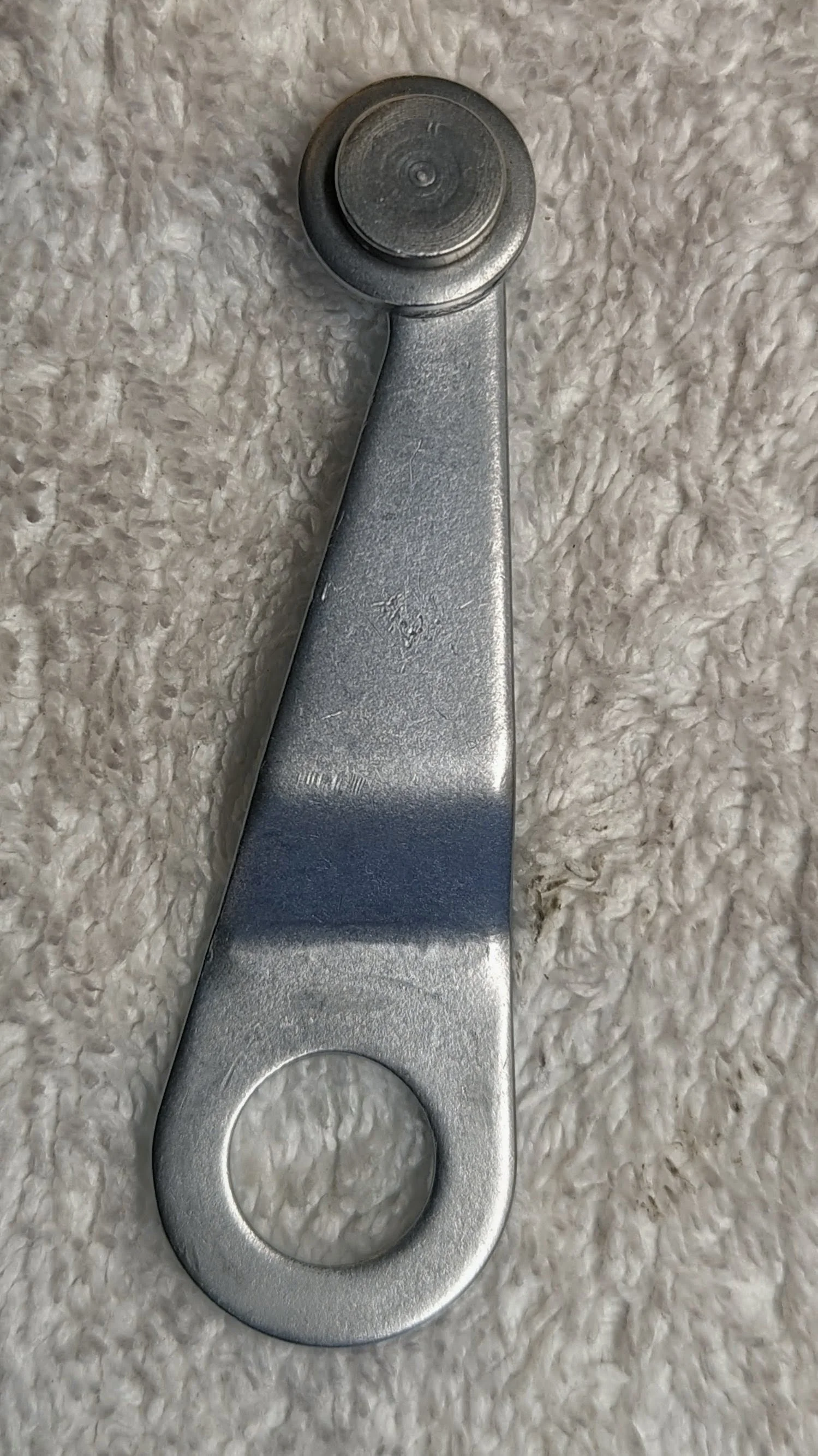 Metal bottle opener lying flat on a textured, off-white surface.