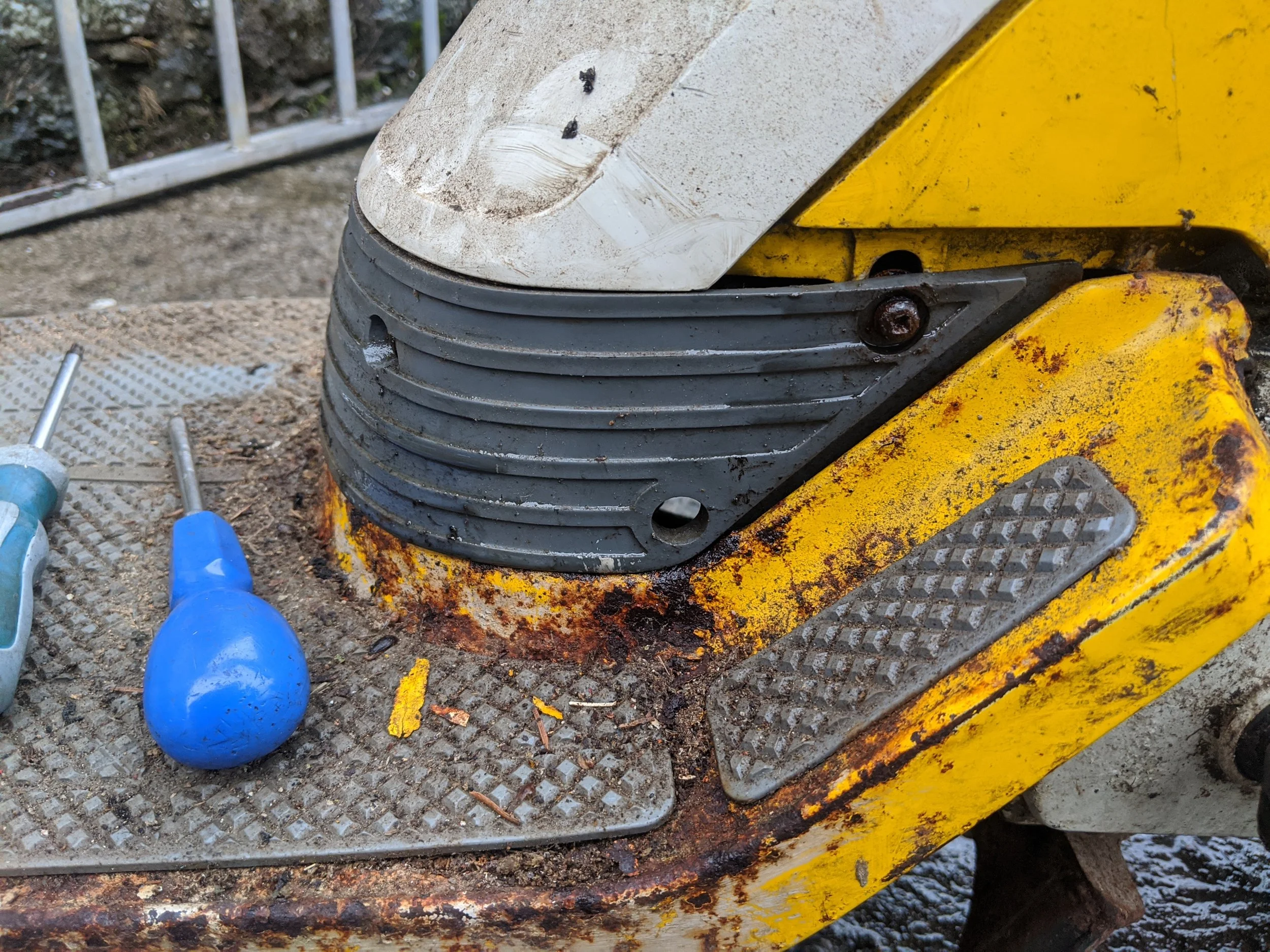 Close-up of a yellow construction machine with dirty white and black parts and tools around on a gravel surface.