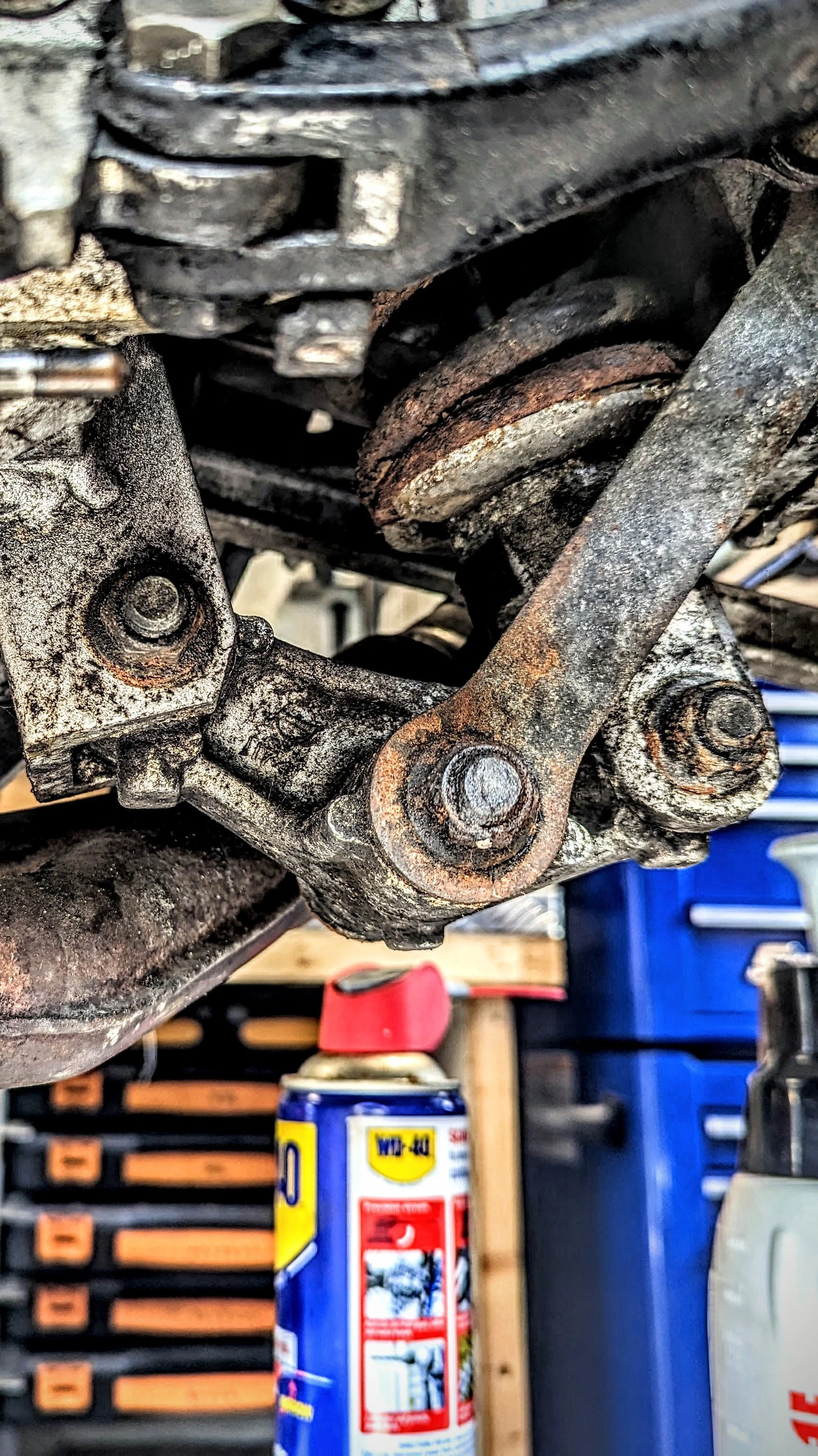 Close-up of a rusty metal motorcycle part with bolts, with WD-40 spray can visible in the background.
