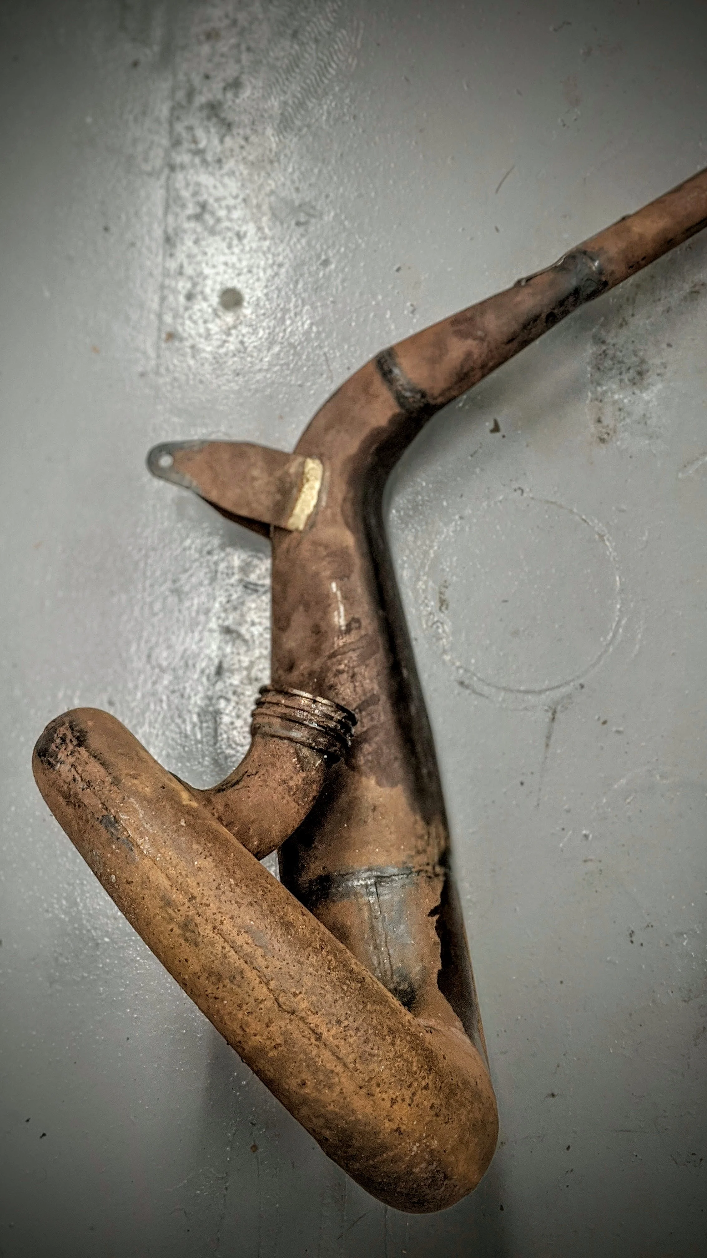An old, rusty pipe or tool with a bent shape and a worn, corroded surface resting on a gray floor.