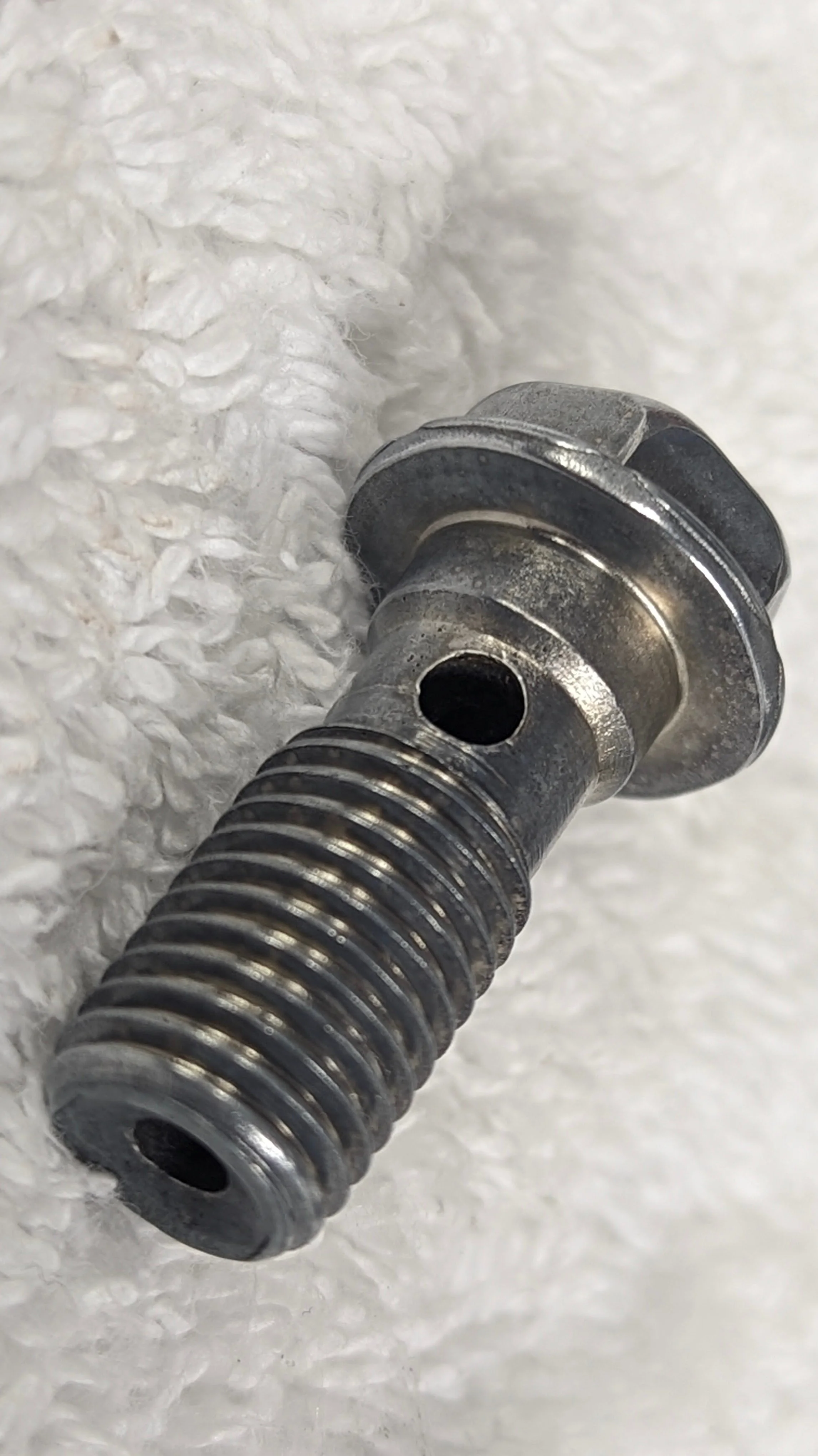 Close-up of a metallic screw or bolt with a threaded shaft resting on white textured paper.