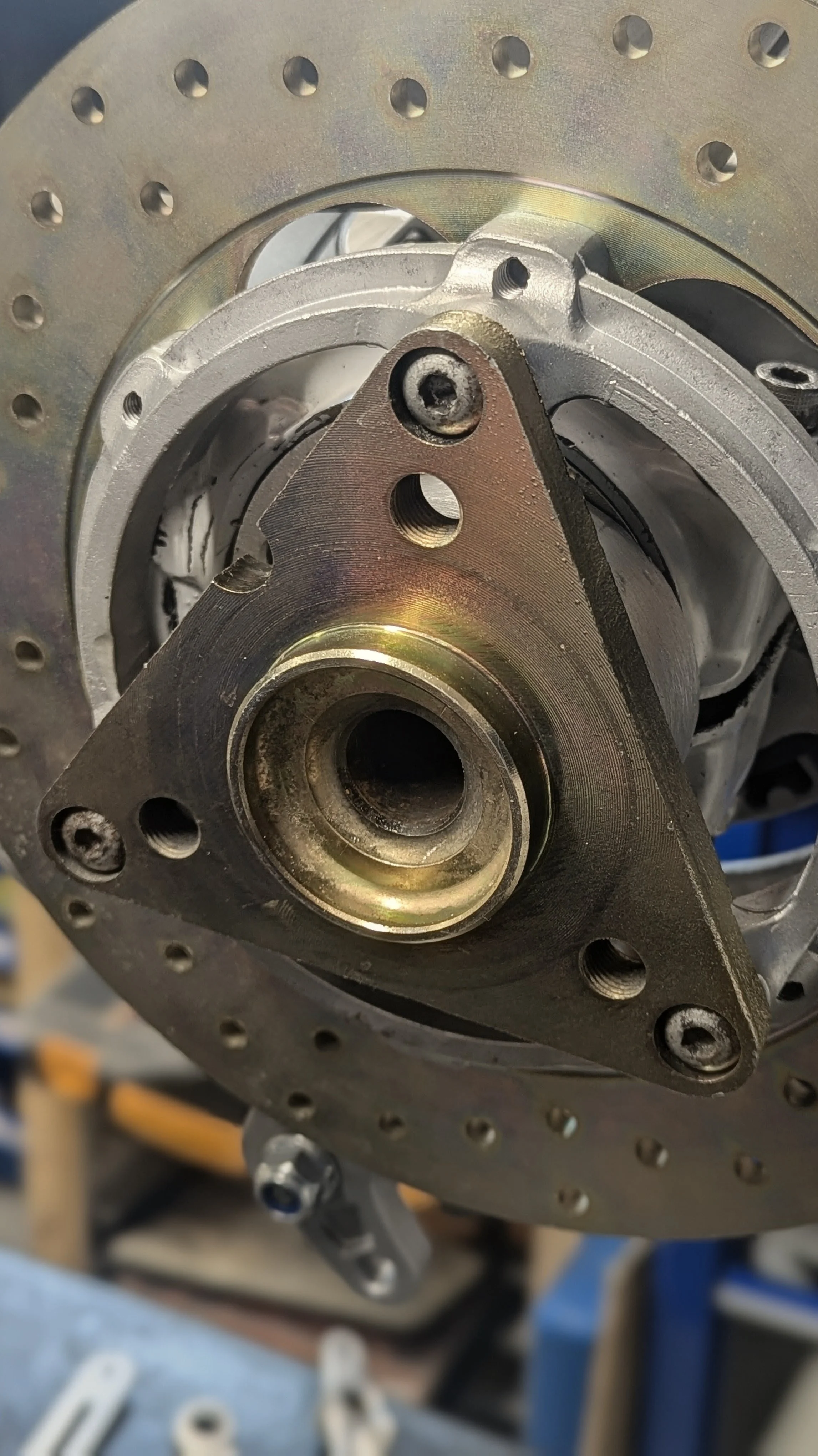 Close-up of a motorcycle engine part with a metallic appearance and several bolt holes, attached to a perforated metal component with a gold and silver finish.