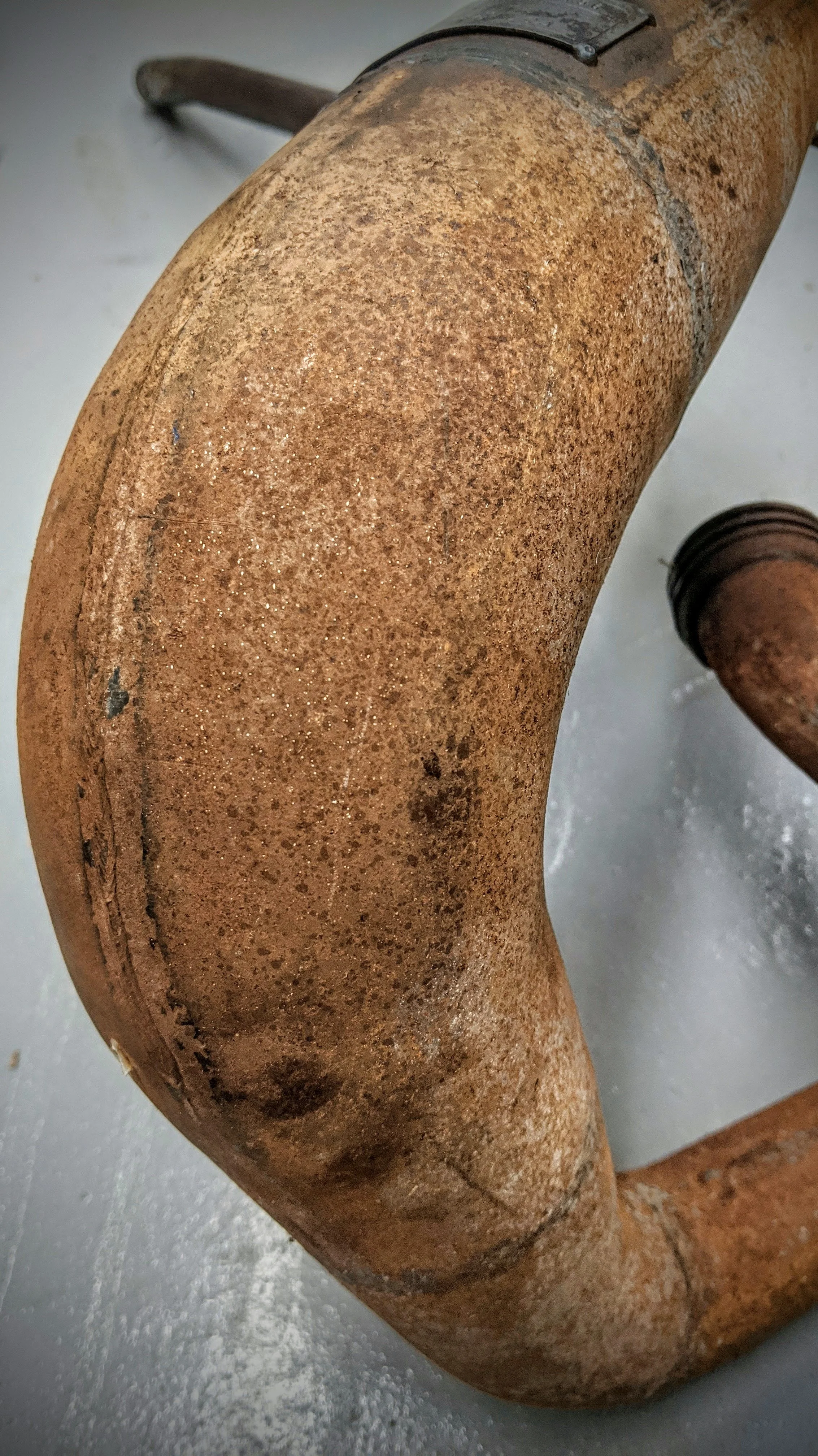 Close-up of a rusty, old metal pipe or elbow fitting on a gray surface.
