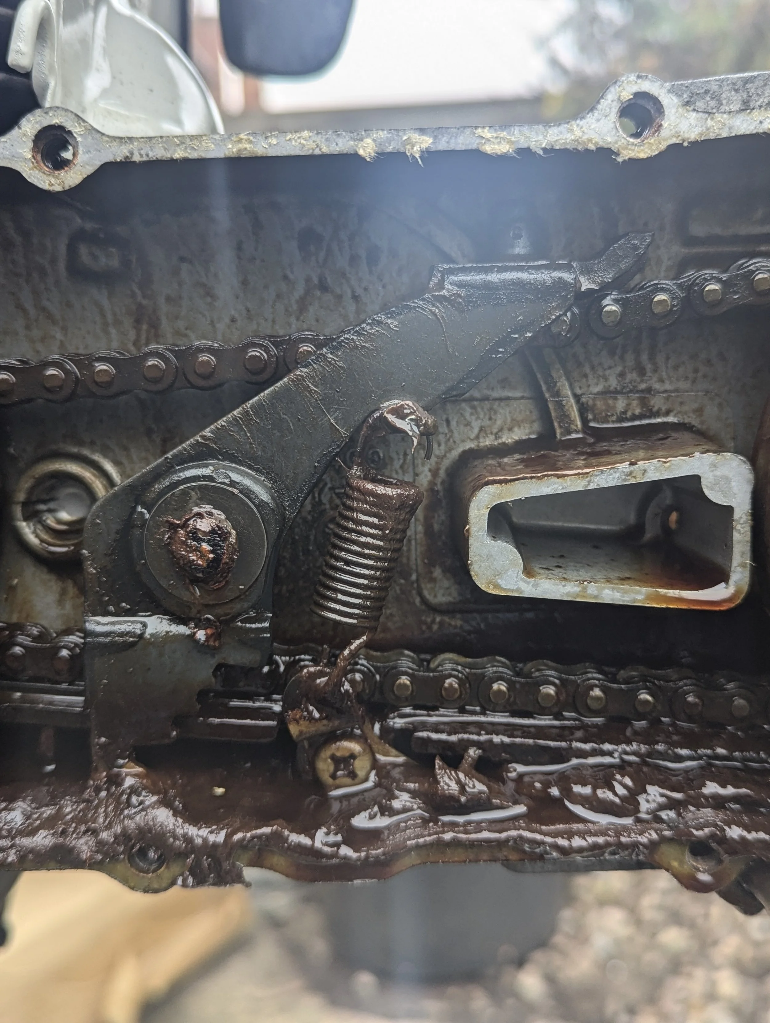Close-up of a dirty, rusty chains and gears on a mechanical part, possibly an engine or machine component.