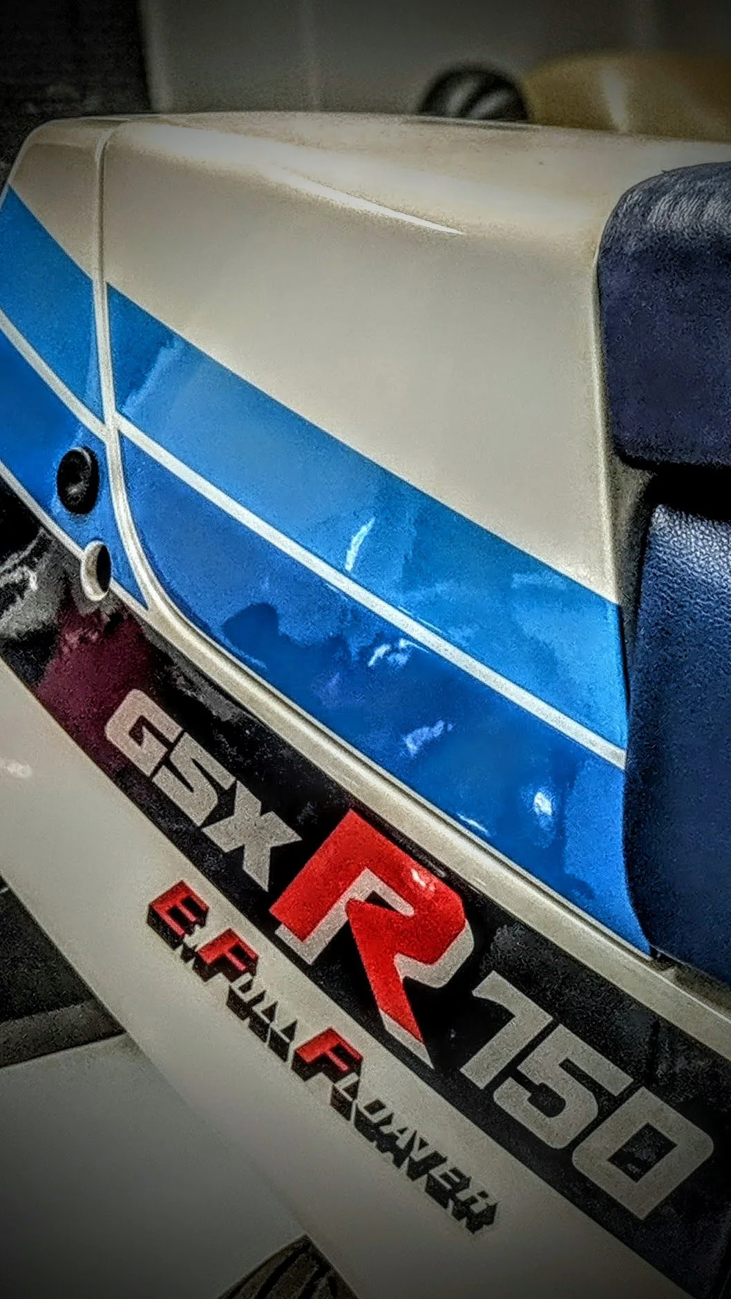 Close-up of a partial view of a vehicle, showing a sticker with the text 'FX,' 'QX,' and 'ERKAER' in black, red, and white colors, and a blue and white section with geometric lines.