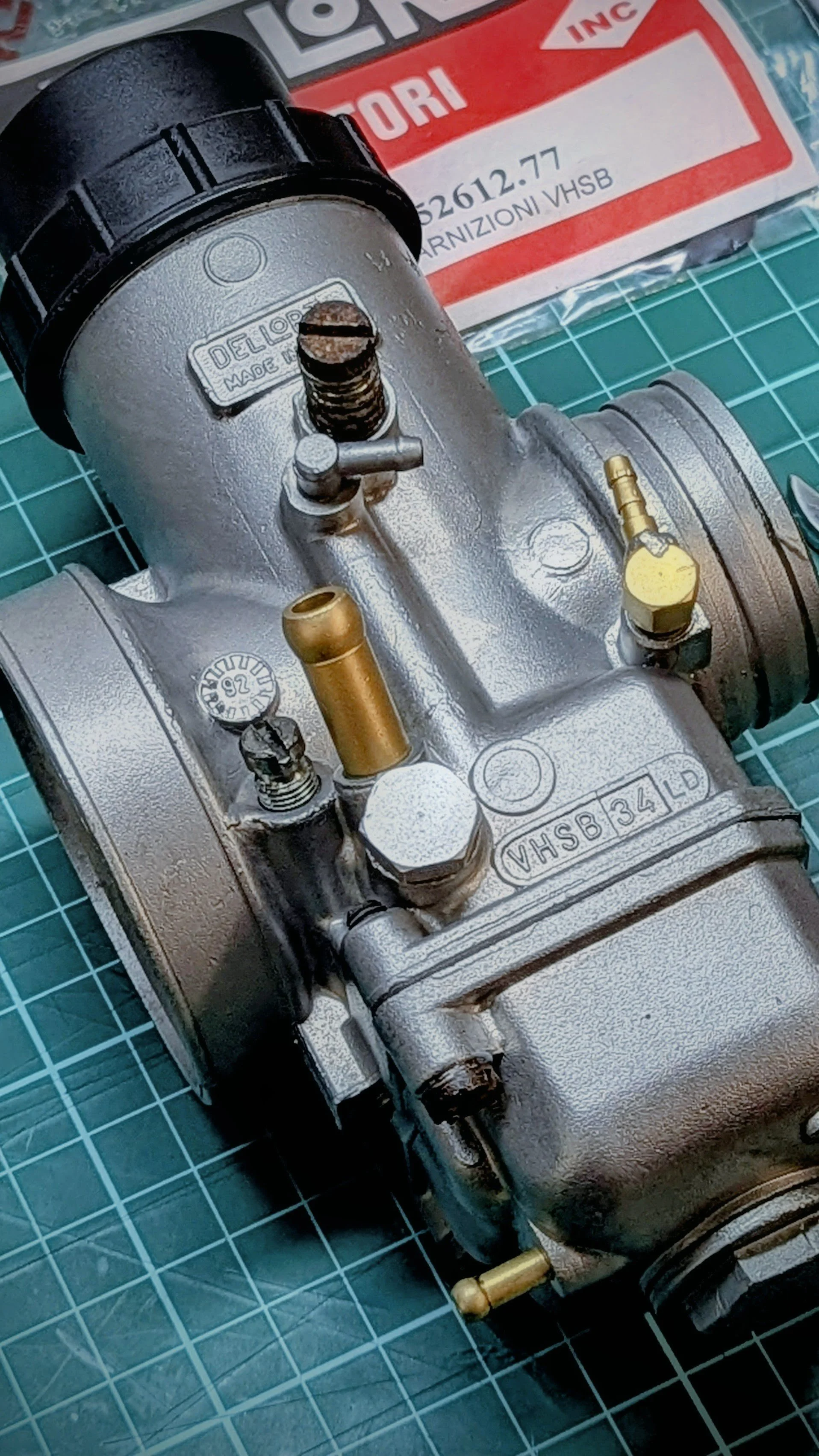 Close-up of a mechanical component with metal parts, screws, and fittings on a green cutting mat, with a red and white sign in the background.