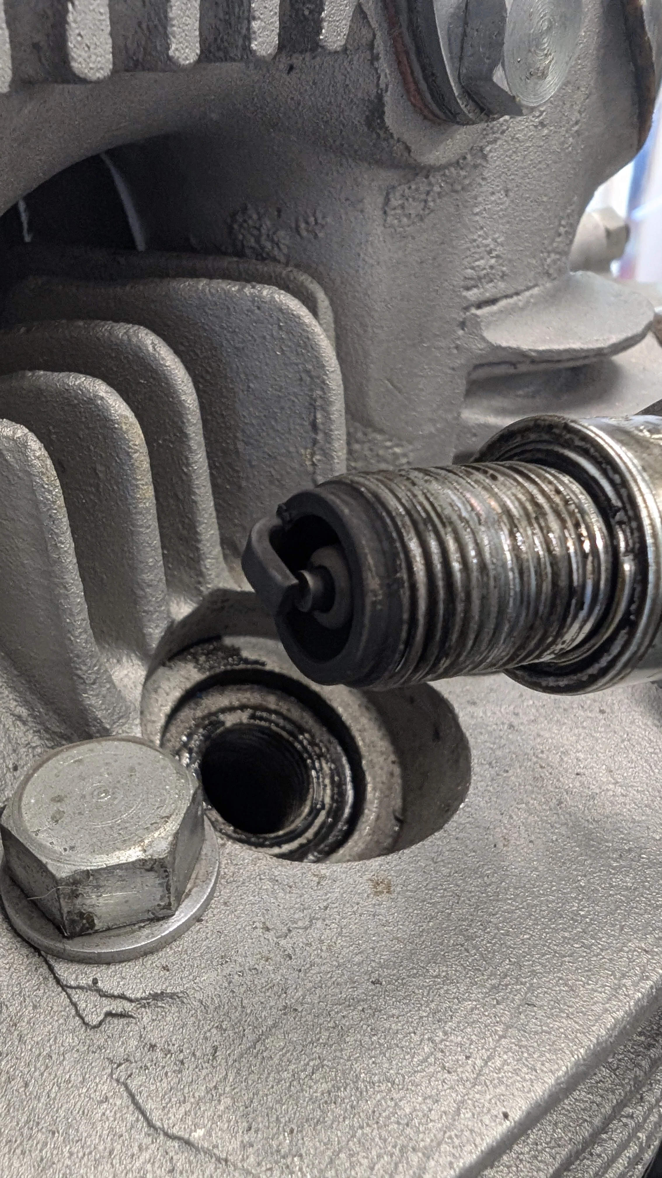 Close-up of an engine component, showing a bolt, a cylindrical metal part, and a textured surface with some oil or grease.