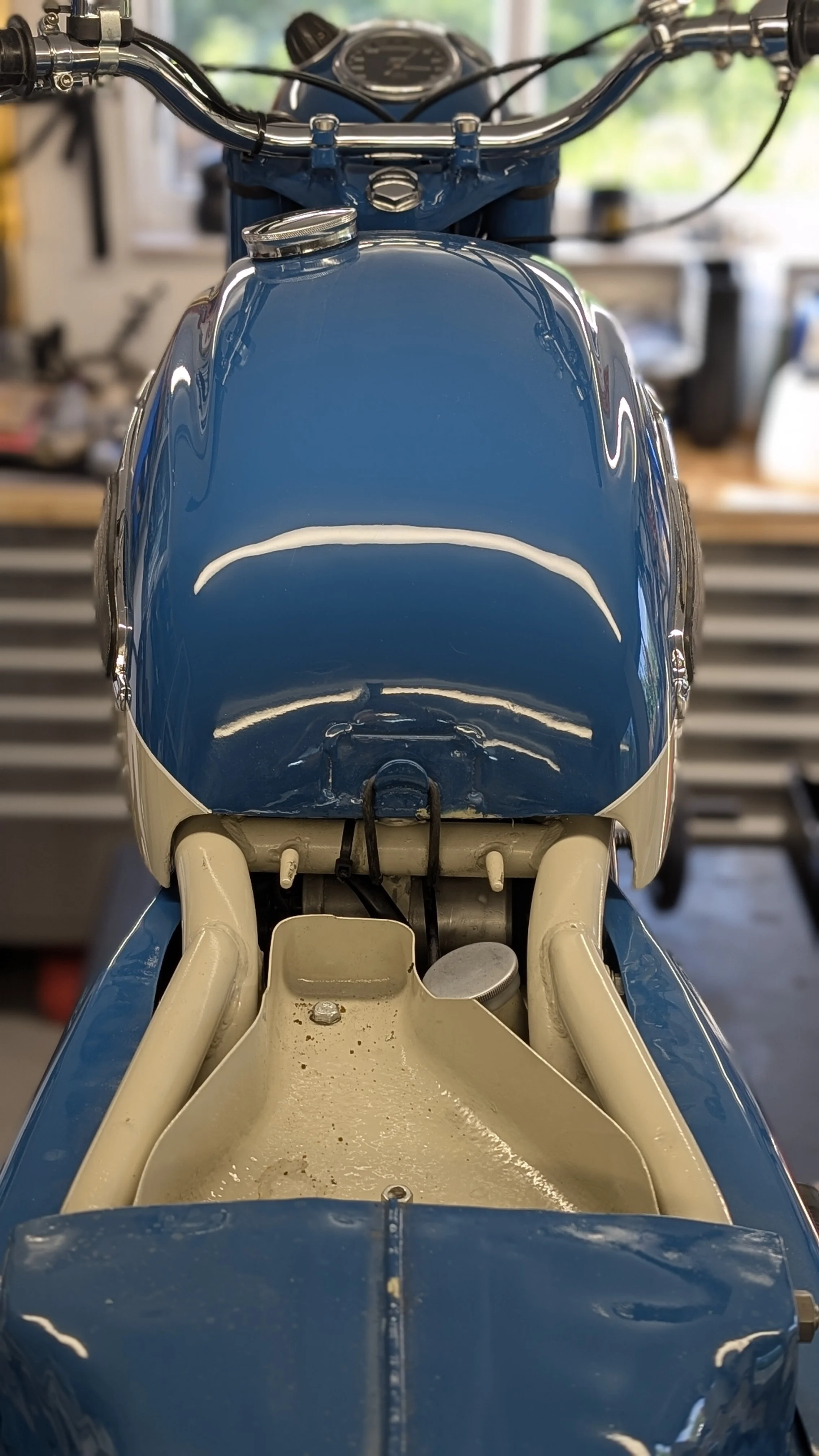 Front view of a vintage motorcycle with a blue and cream color scheme, showing the fuel tank, handlebars, and empty seat area.