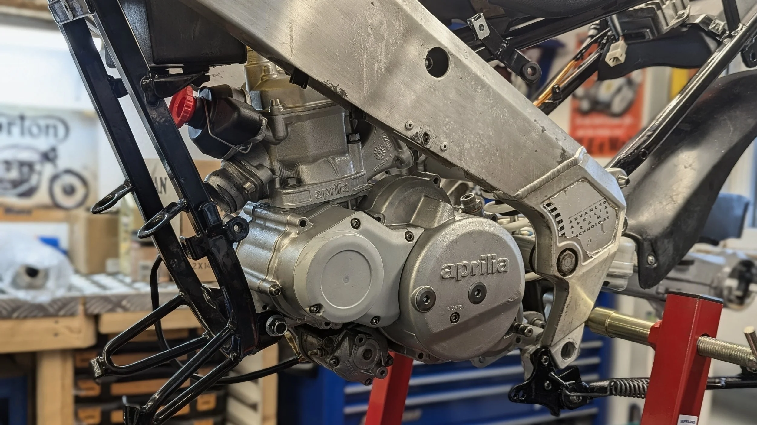 Close-up of a motorcycle engine and frame under construction, with tools and workbench in background.