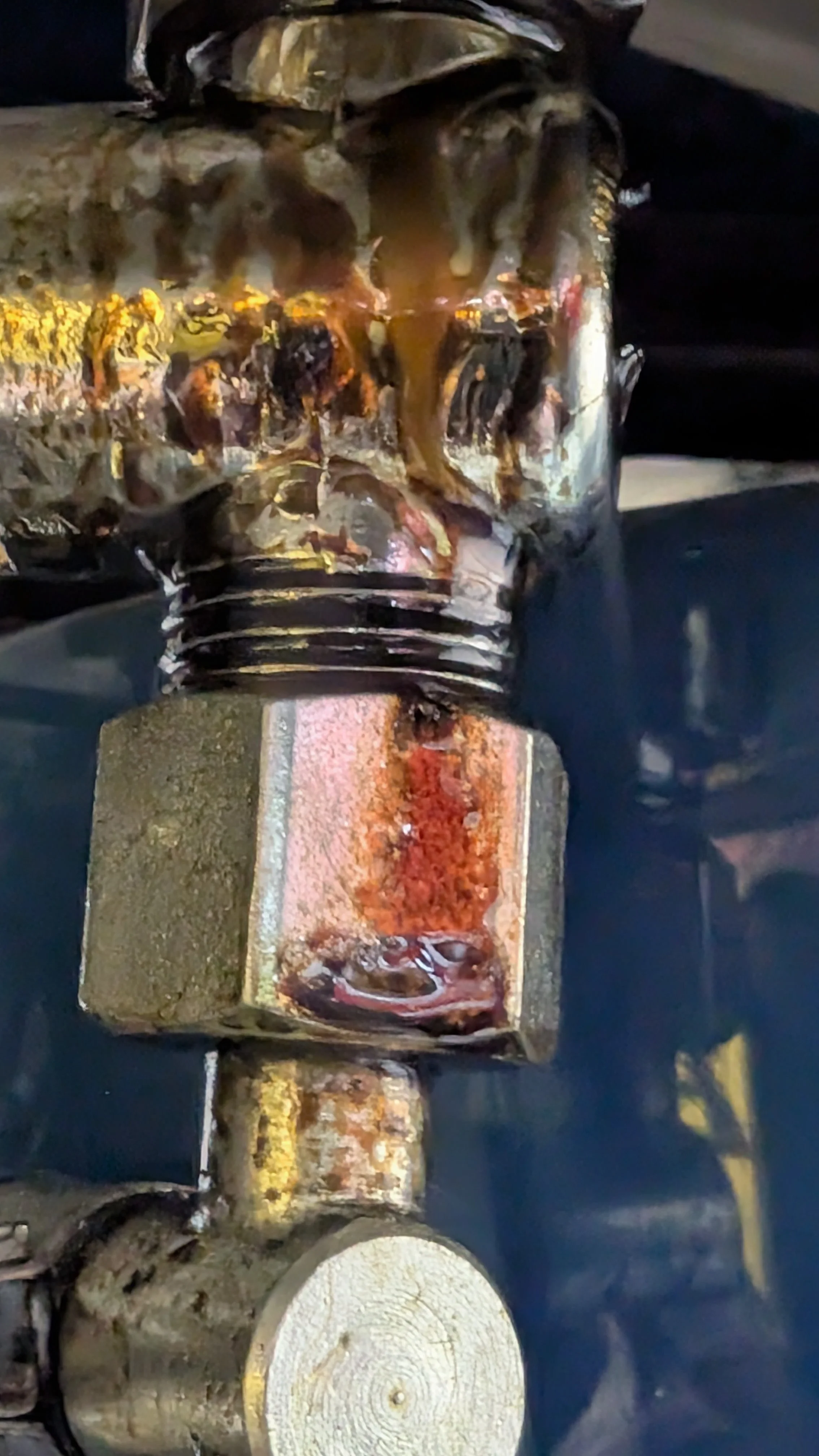 Close-up of a rusty metallic bolt on a machine machine part with a chain and a wooden log in the background.
