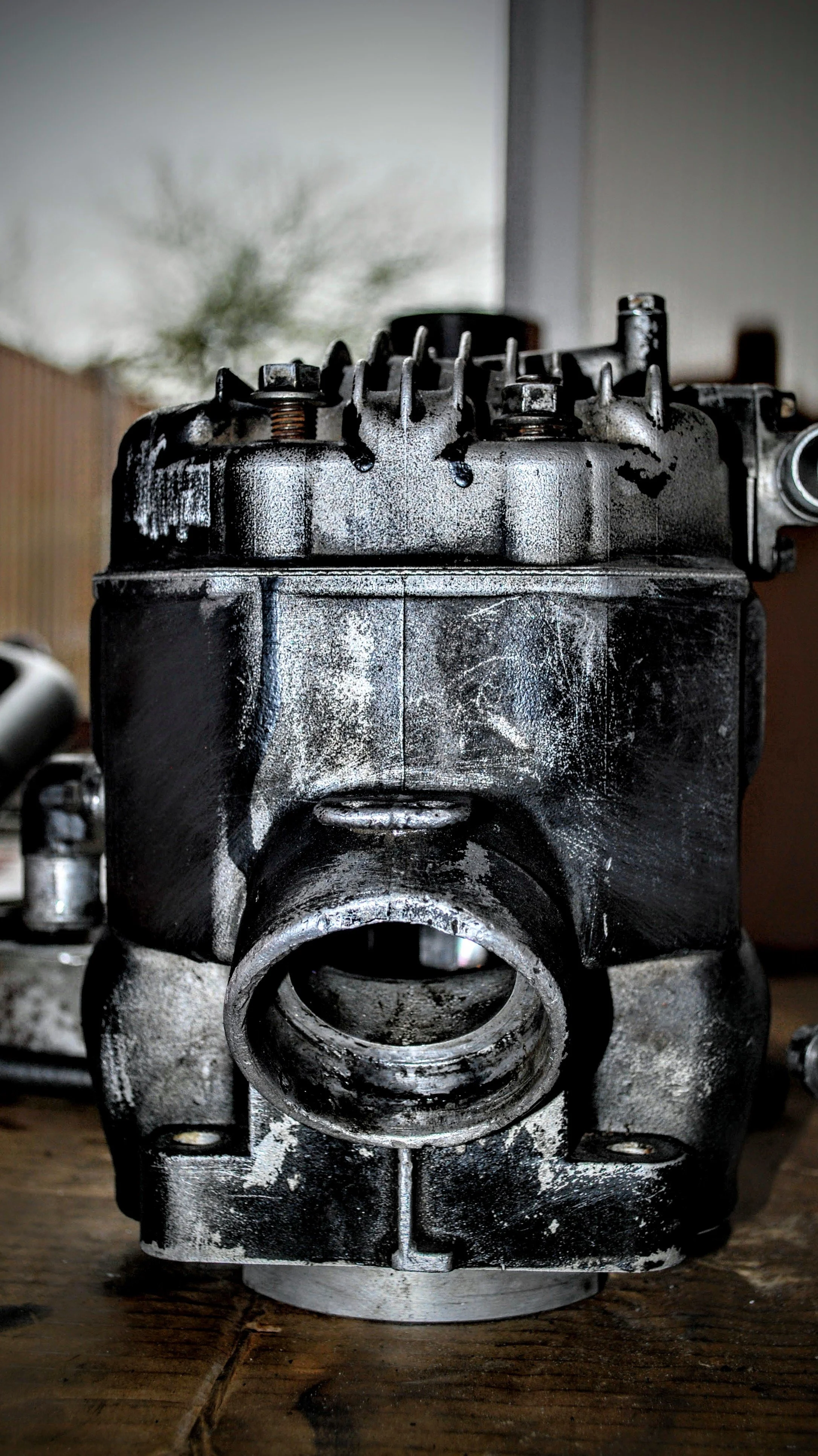 Close-up of a damaged and dirty engine block with scratches and oil stains, placed on a wooden surface.