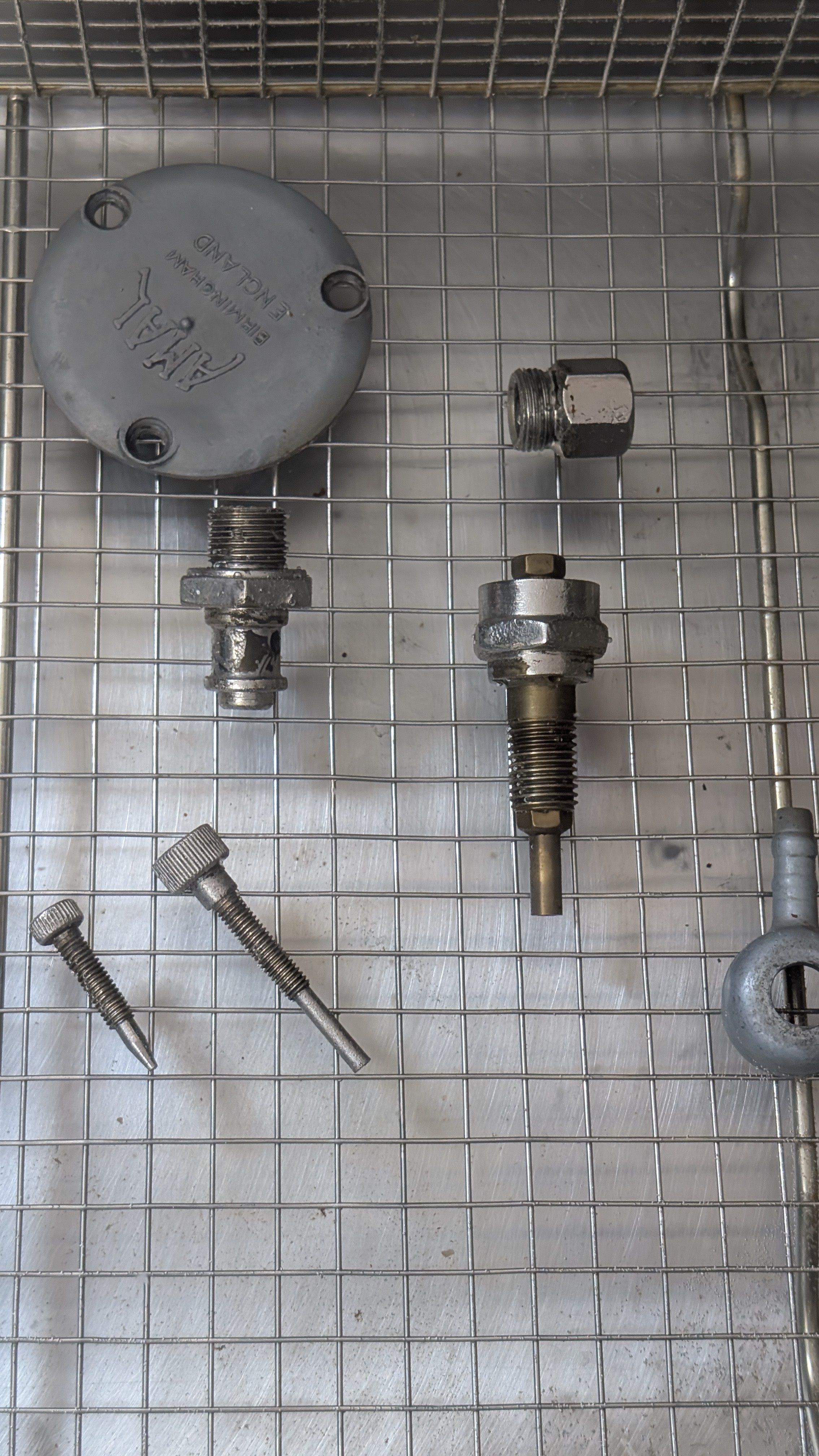 Metal mechanical parts and screws on a wire grid surface.