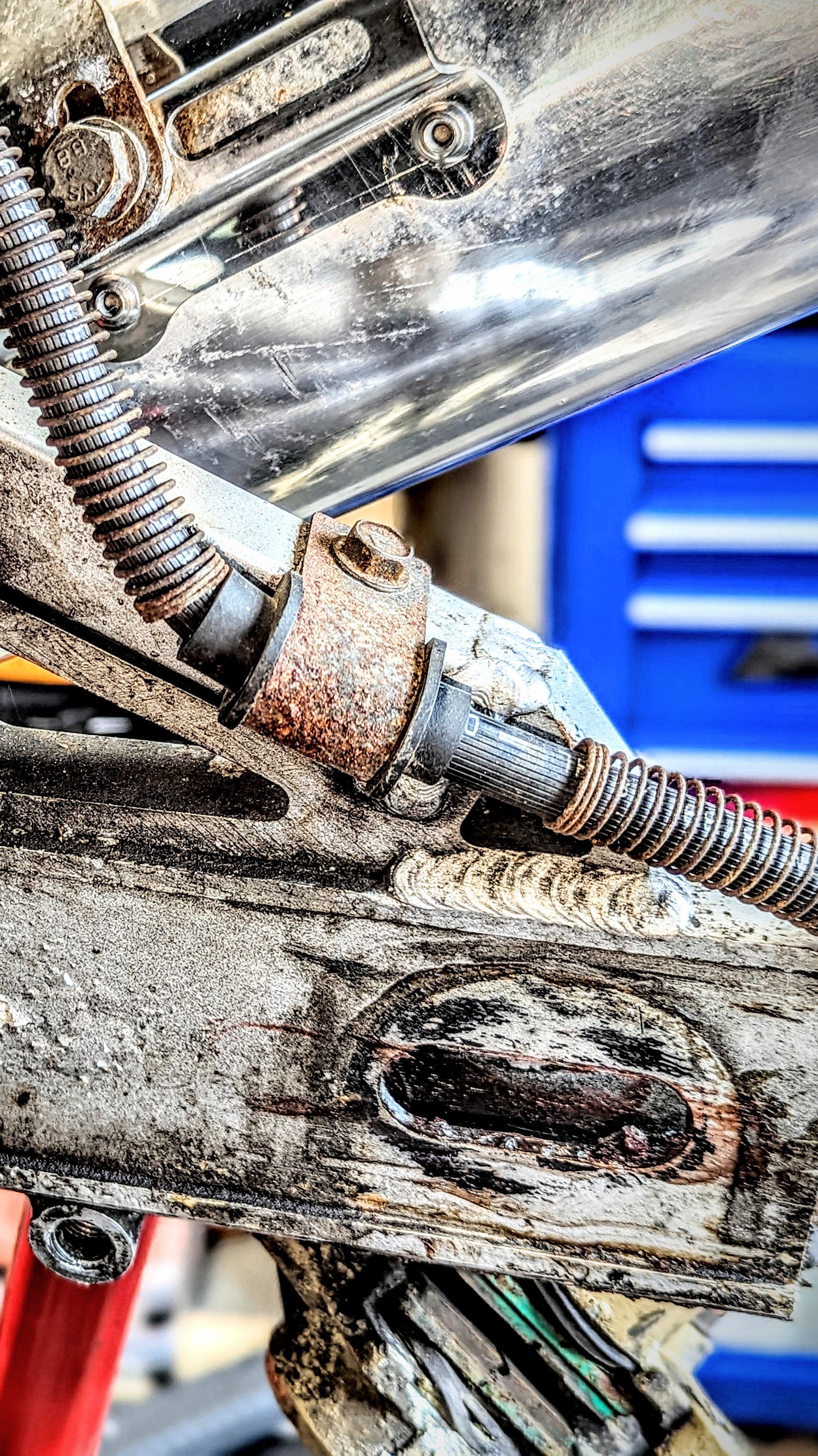 Close-up of a rusty mechanical part with springs, bolts, and metal components, appearing to be part of a machine or engine fixture.