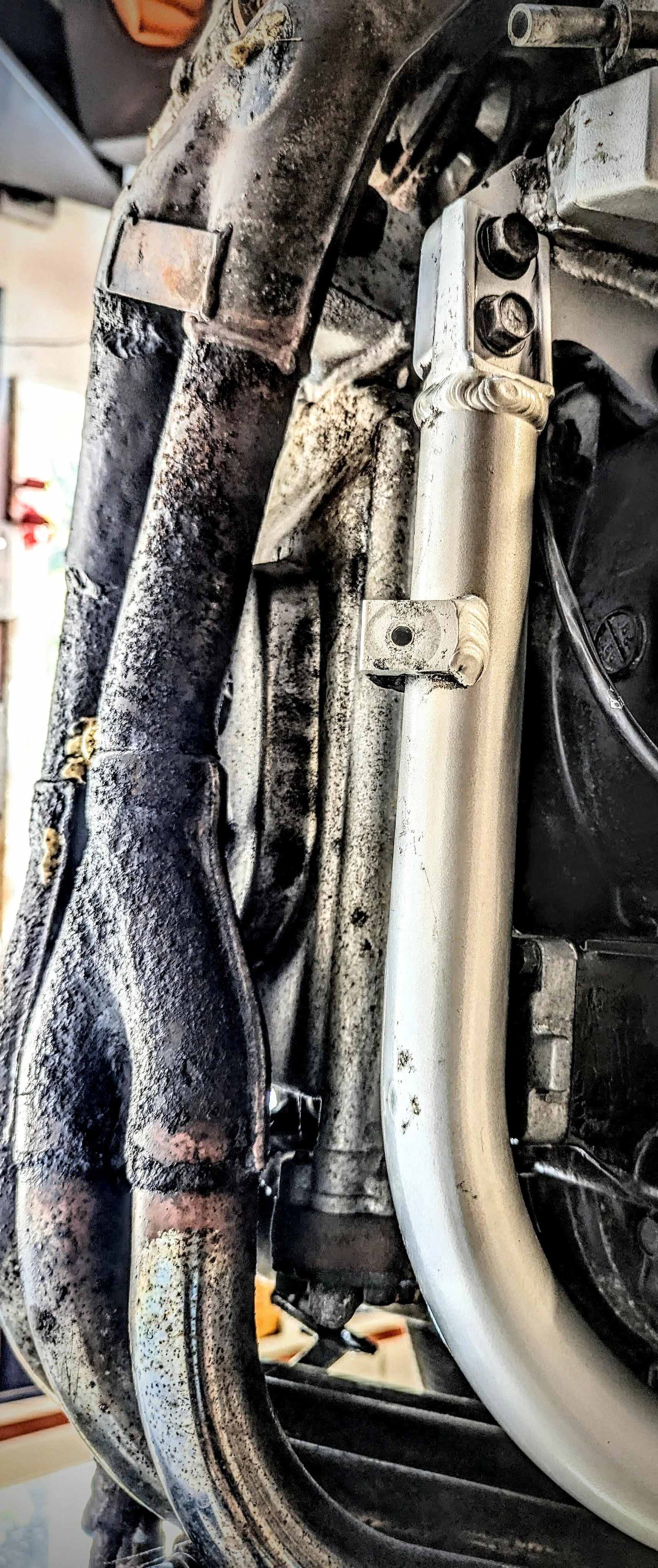 Close-up of dirty metal pipes and a white cylindrical component with bolts, part of a machine or engine.
