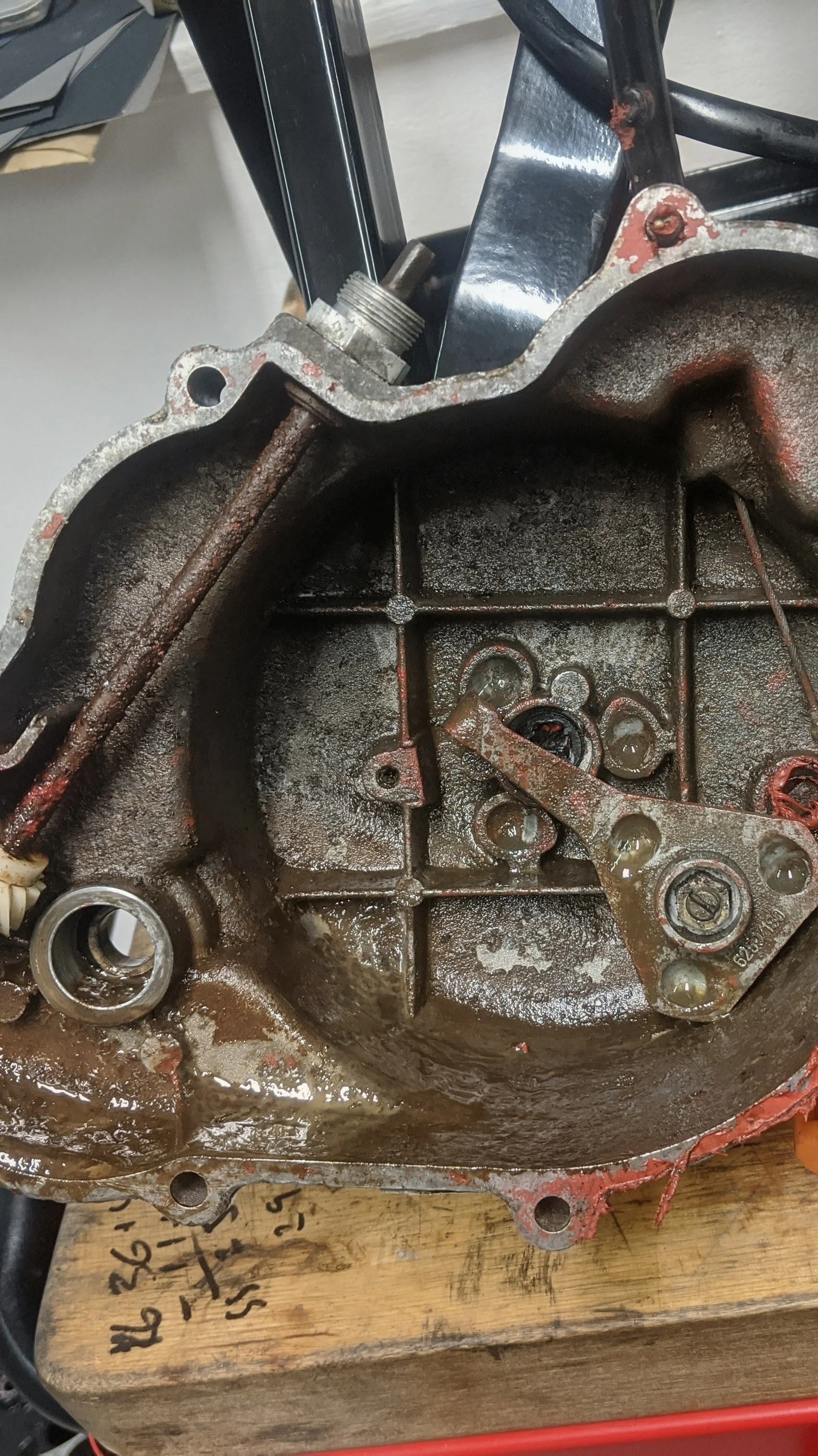 A close-up view of an engine housing with some internal components and oil residue, resting on a wooden work surface.