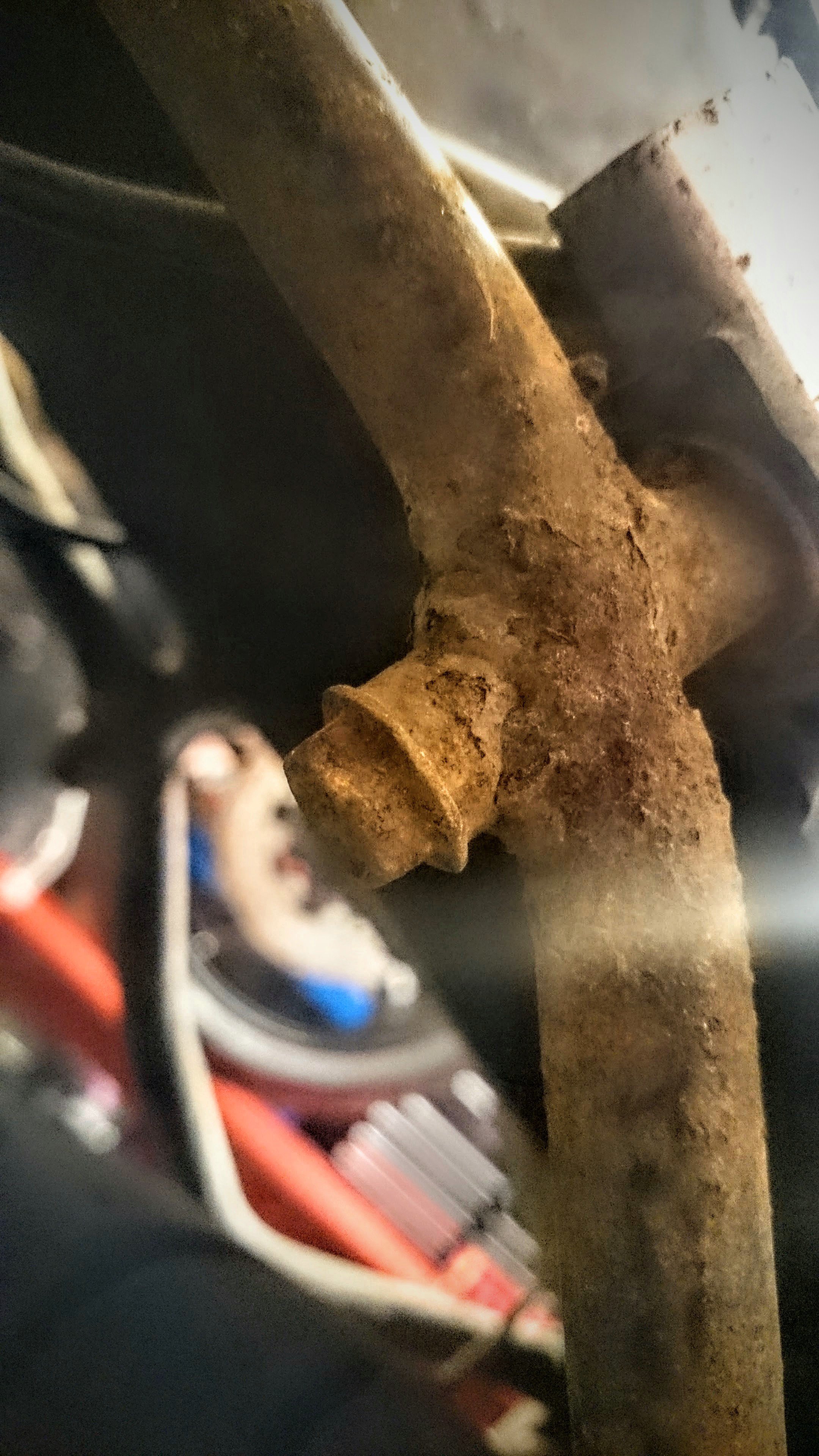 Close-up photograph of a rusty, corroded metal bolt or axle in an automotive or machinery component with visible electrical wiring nearby.