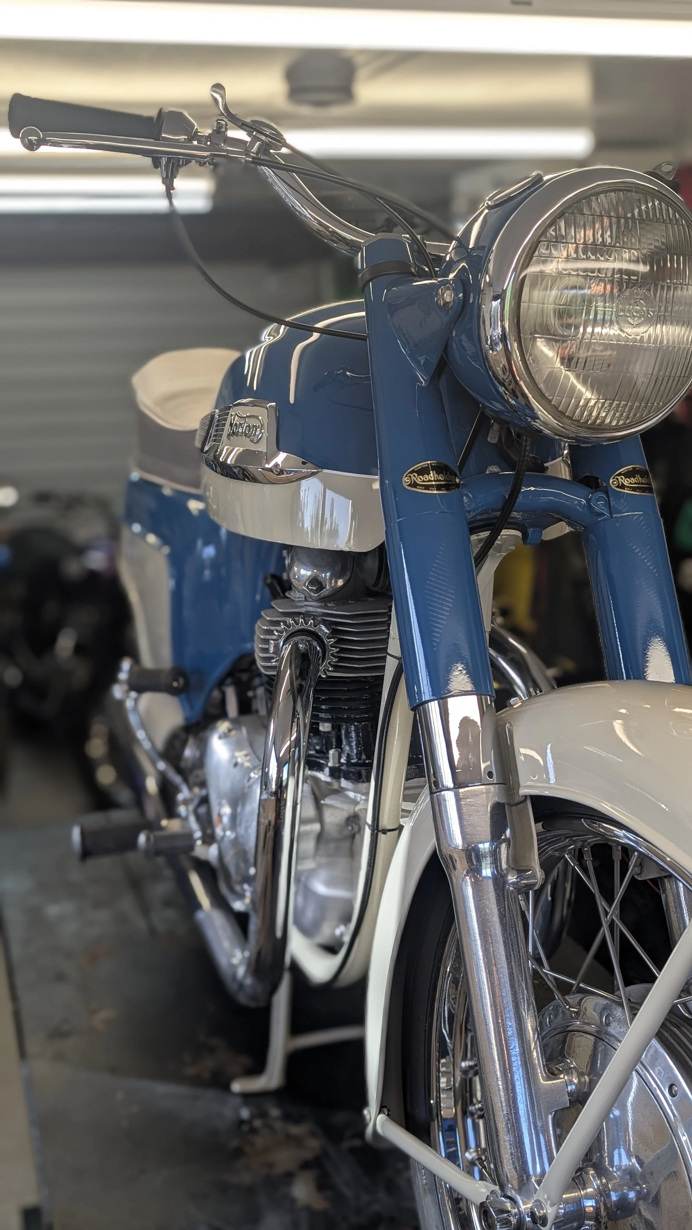 Close-up of a vintage blue and white motorcycle in a workshop or garage.