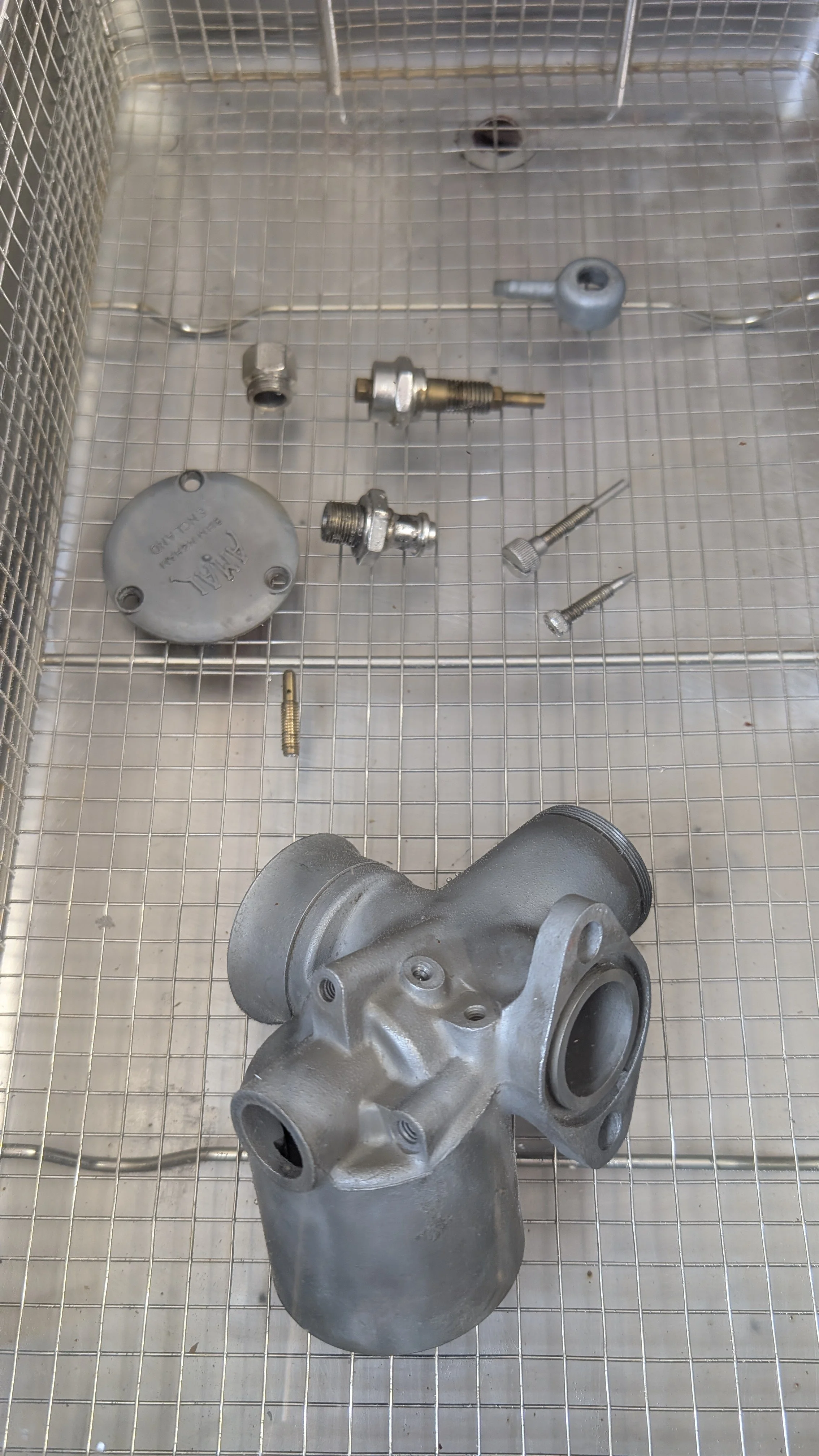Metal automotive parts including a housing, valves, and screws laid out on a wire grid surface.