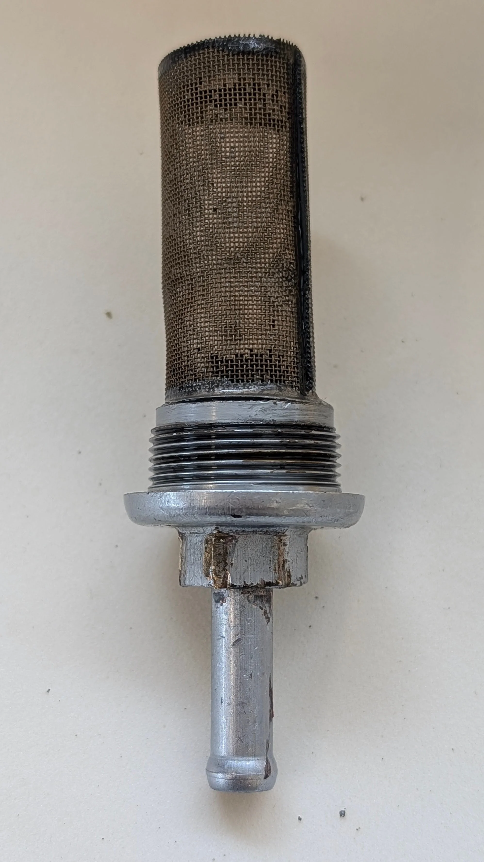 Close-up of a metallic automotive or mechanical sensor with a mesh covering, threaded body, and protruding metal rod against a plain background.