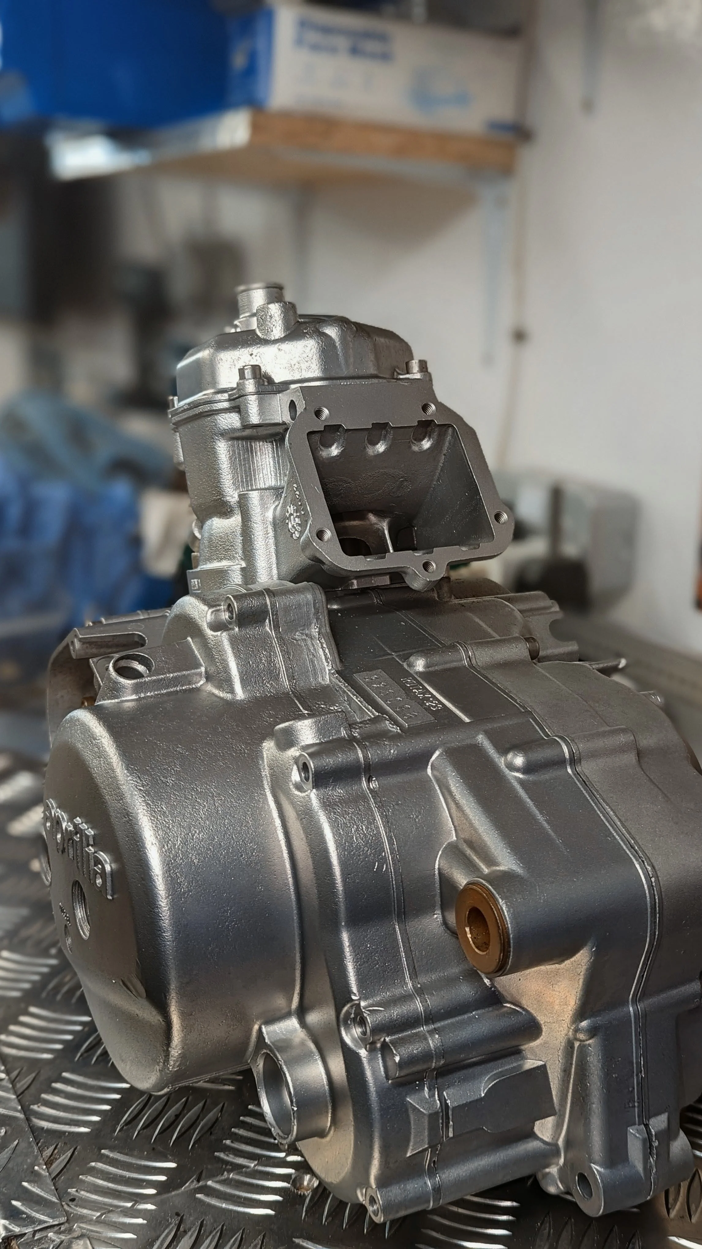 A metallic engine or mechanical component with a black gasket or cover, placed on a metallic work surface in a workshop.