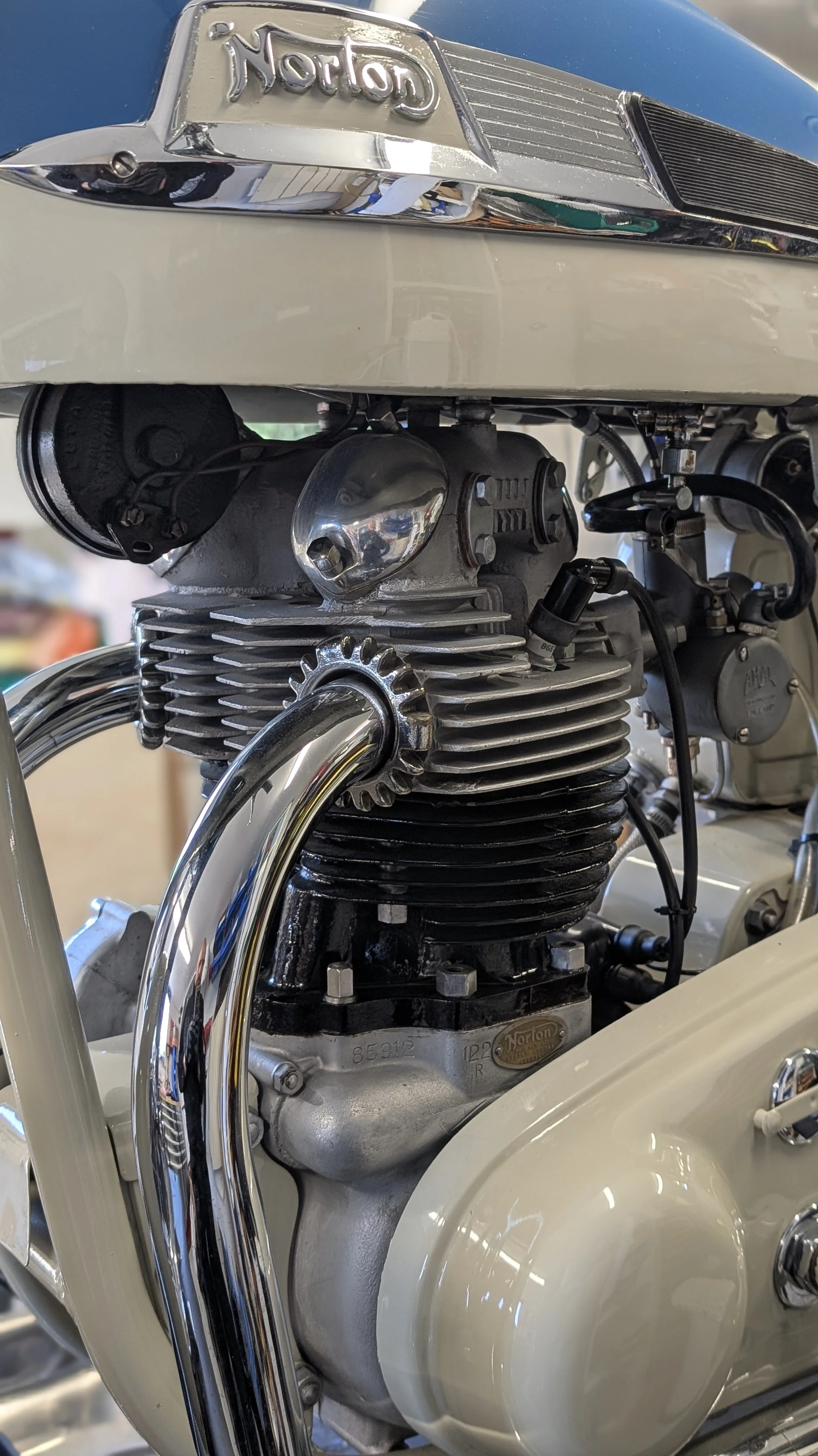 Close-up of a vintage motorcycle engine with a Norton badge, chrome pipes, and a cream-colored body.