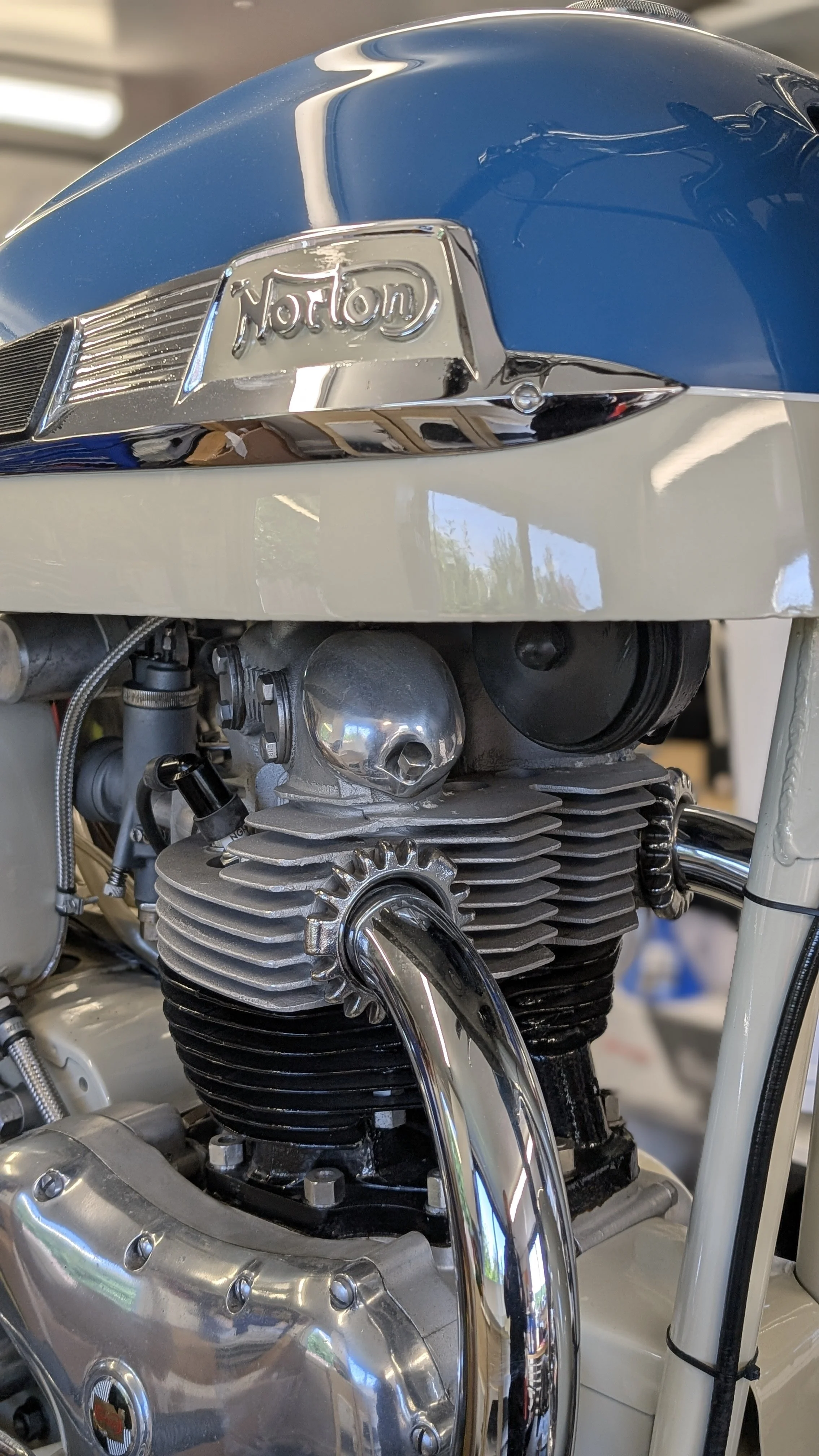 Close-up of a vintage motorcycle engine and a blue and white gas tank with a chrome emblem that says Norton.