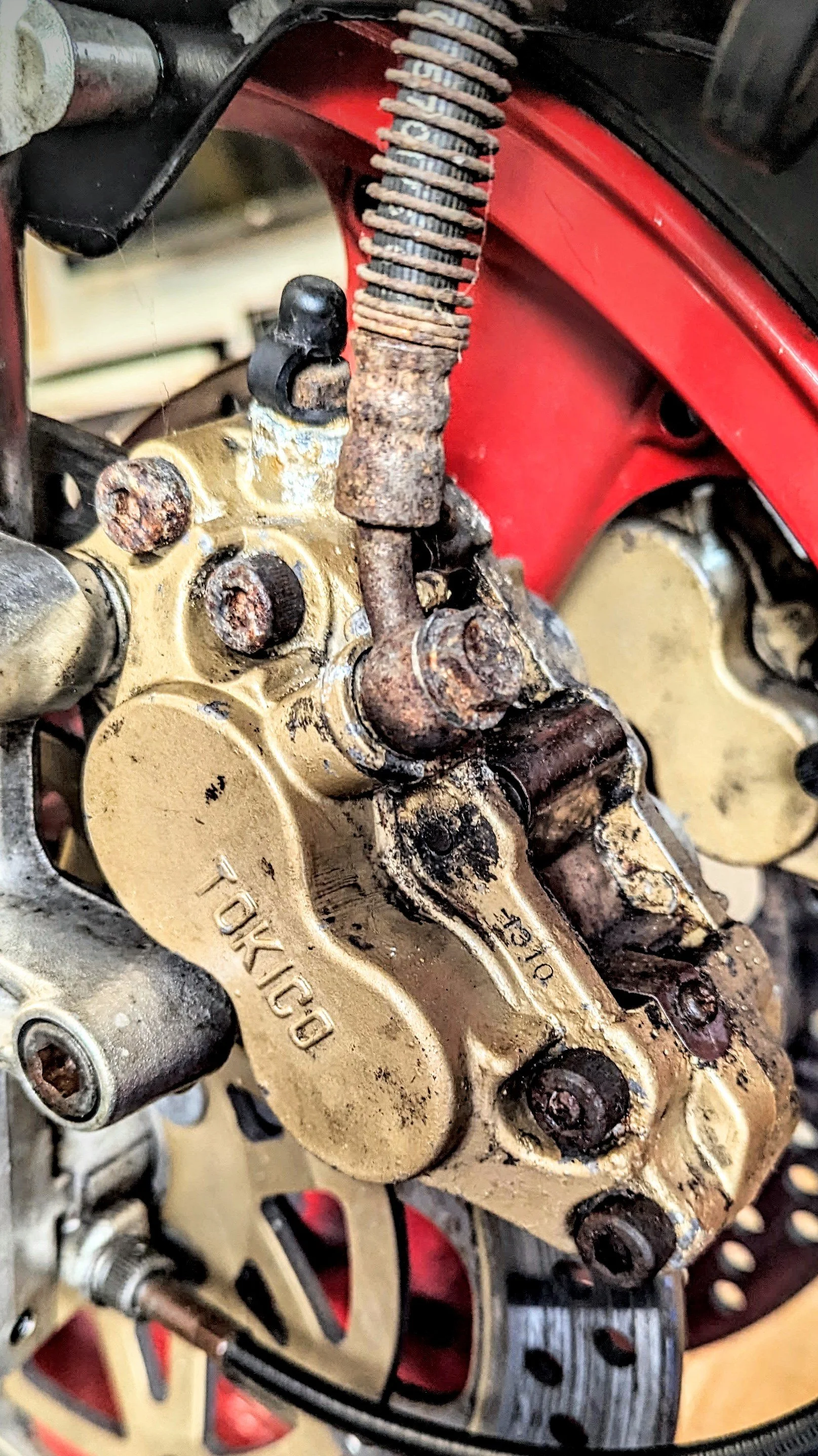 Close-up of a rusty motorcycle engine component with a coil spring and a red frame in the background.
