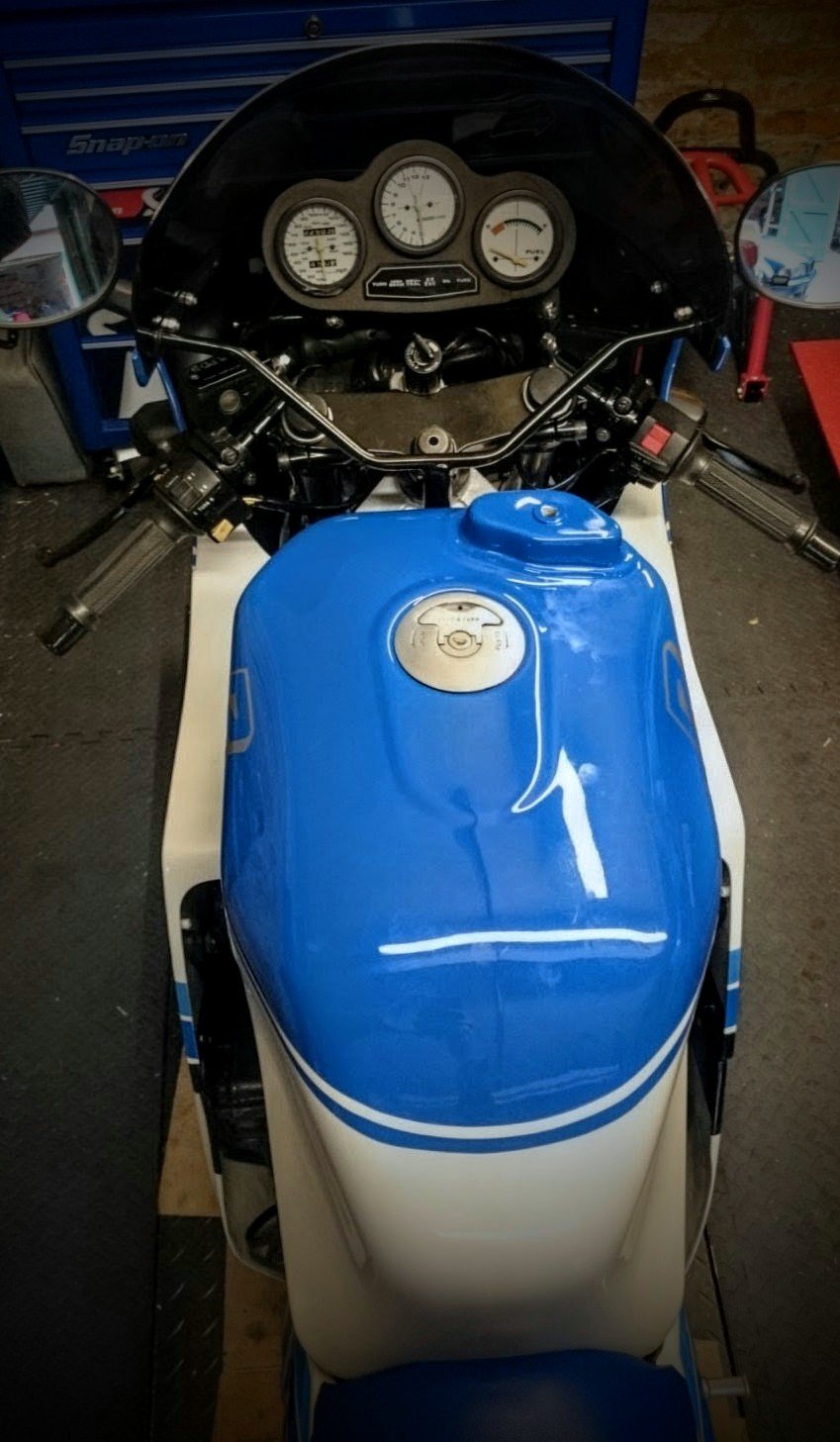 Top view of a blue and white motorcycle with a black windscreen, handlebar controls, and a dashboard with three gauges.