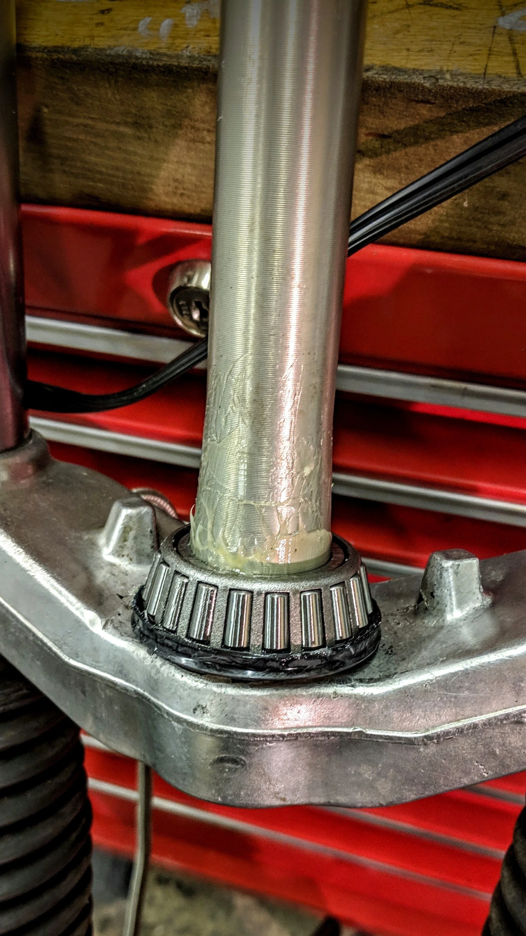 Close-up of a motorcycle front fork with a damaged bearing and a red tool chest in the background.