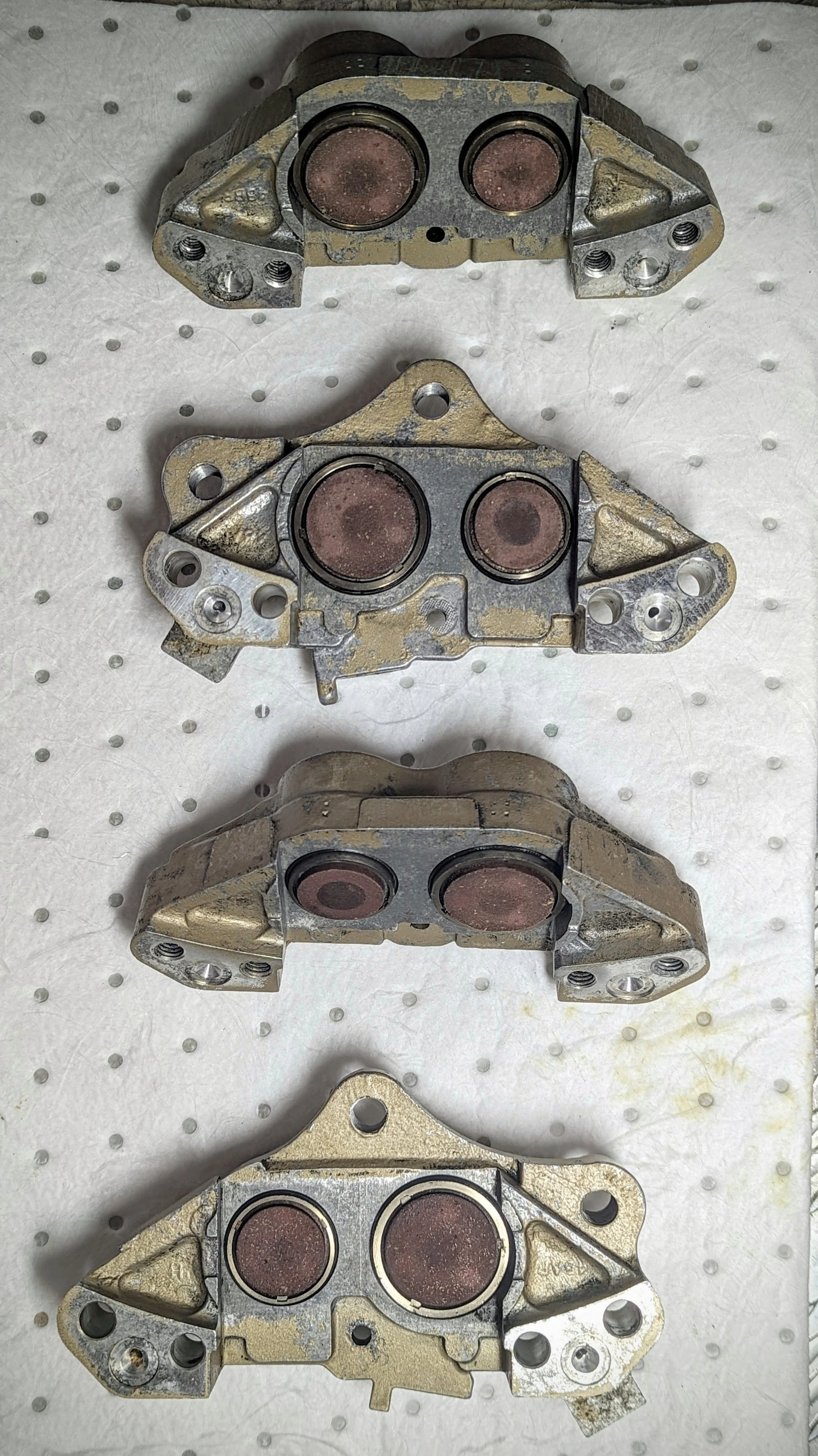 Four car engine cylinder head components lined up on a white perforated surface, showing the intake and exhaust ports.