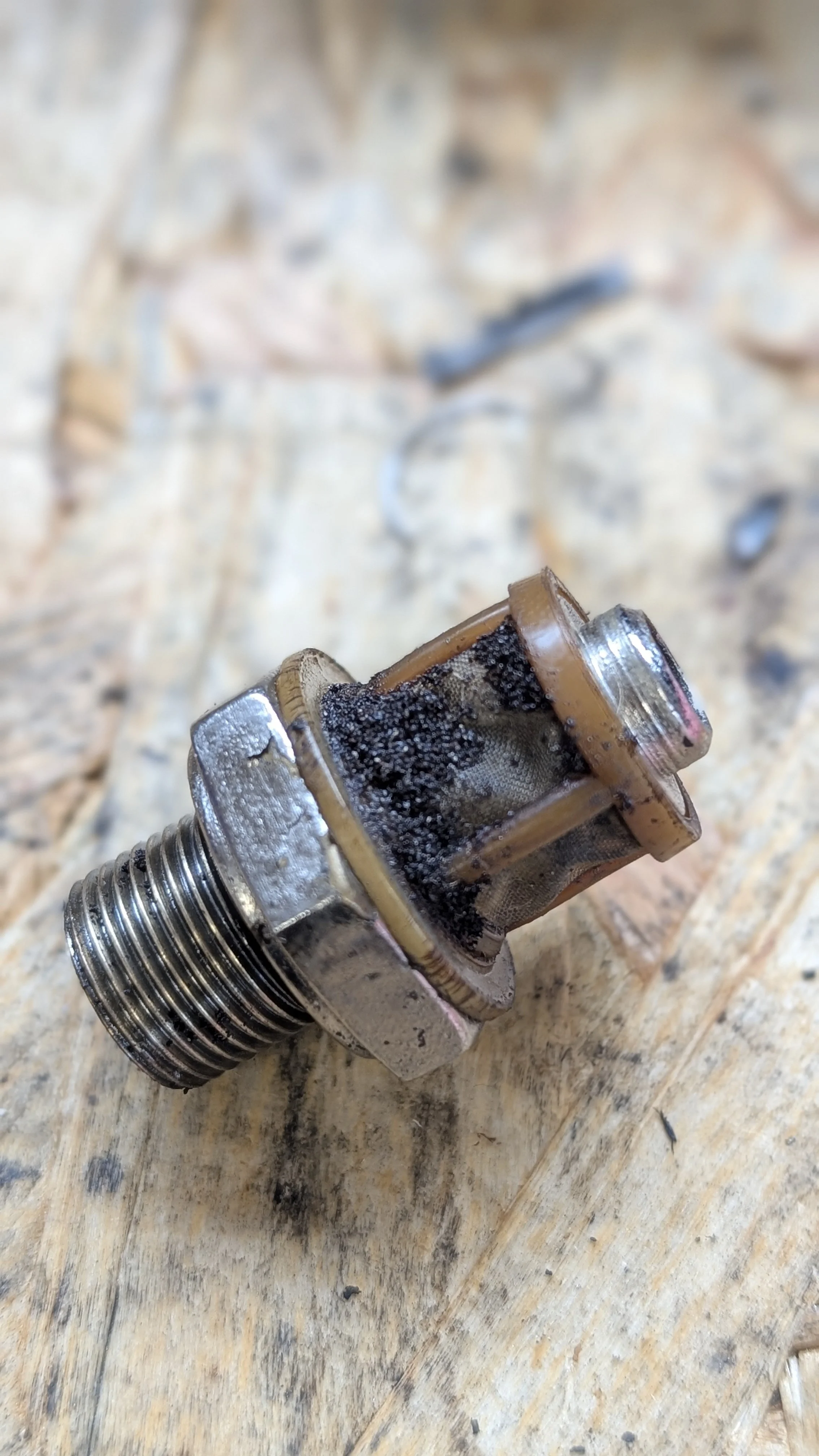 A worn and dirty spark plug lying on a wooden surface.