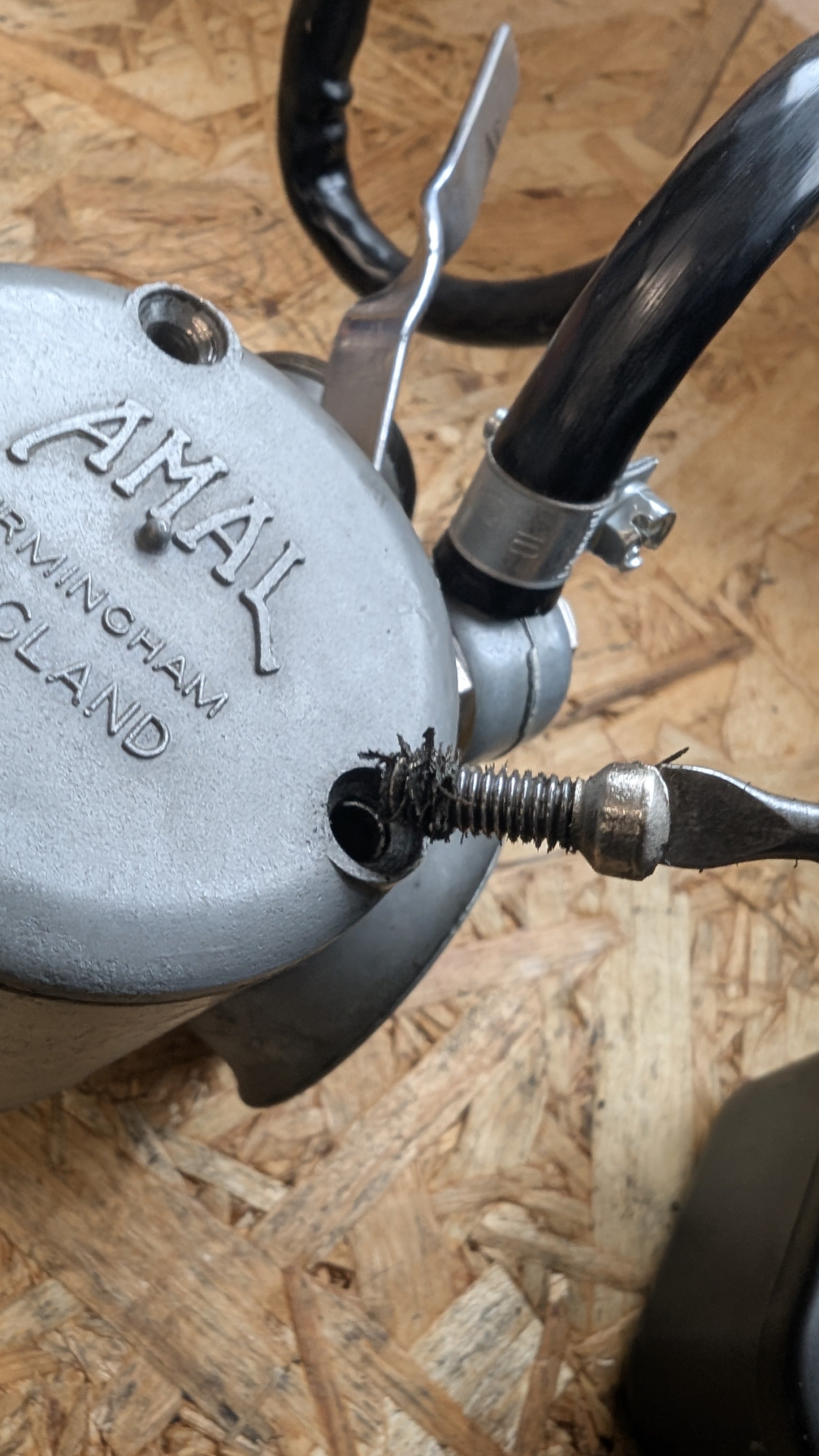 Close-up of a vintage motor or machinery part with a visible textured gray surface, a rusted screw, and black metal pipes, on a wooden floor.