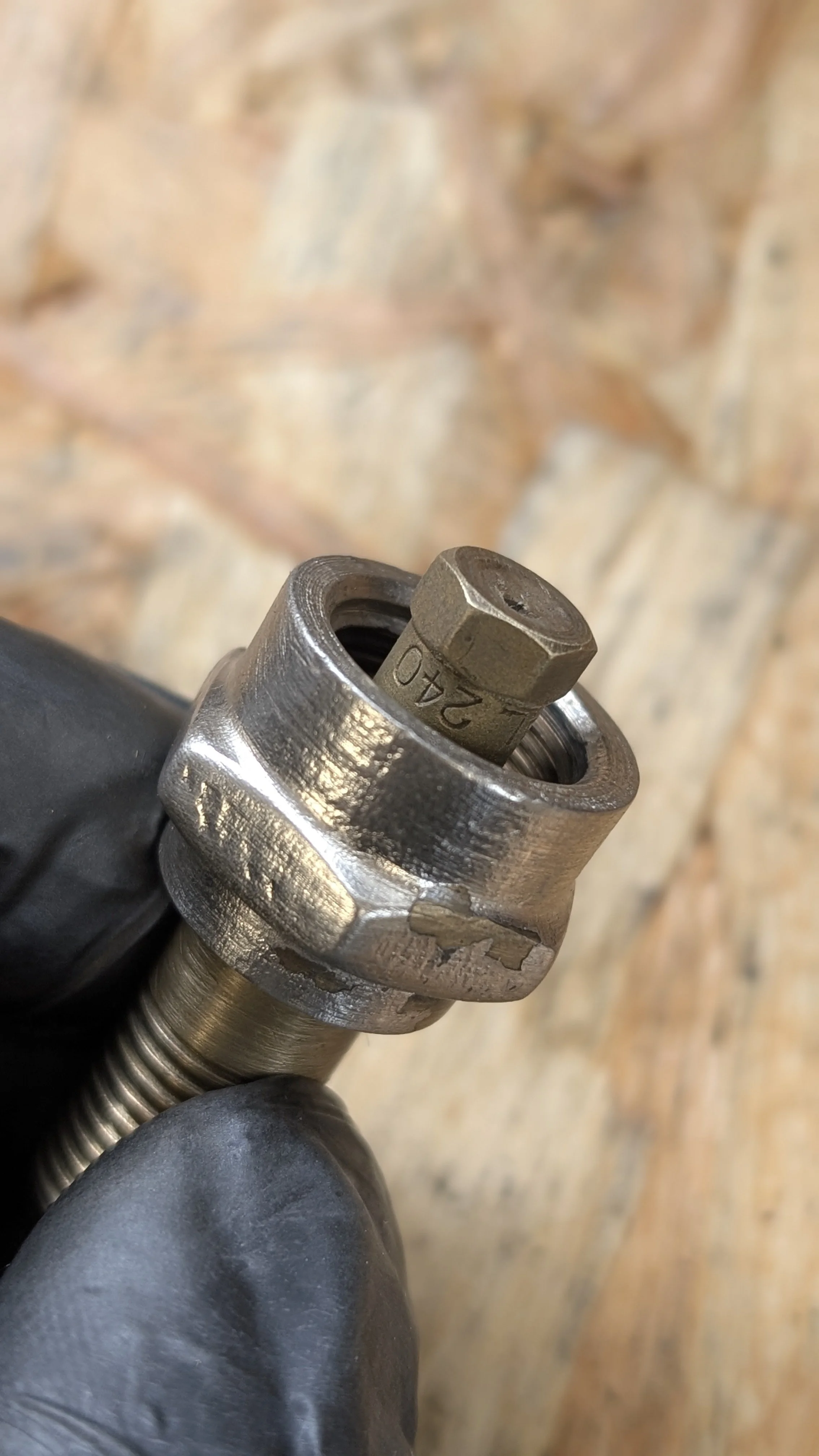 Close-up of a metal mechanical part with a notable marking of '240' on the central bolt, held by a person in a black glove.